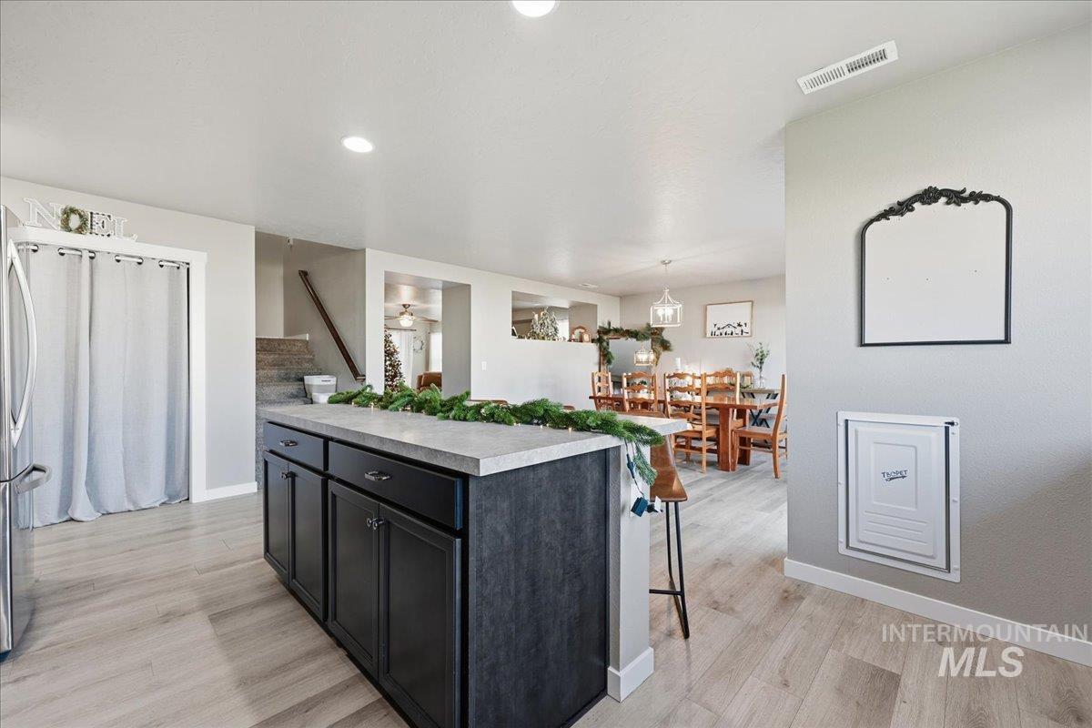 Kitchen featuring dark cabinets, stainless steel fridge, light wood-style flooring, hanging light fixtures, and recessed lighting