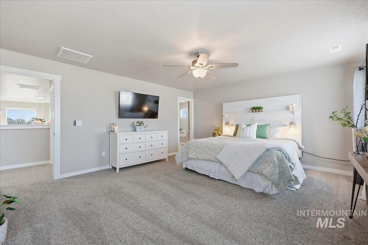 Bedroom with light colored carpet, ceiling fan, and connected bathroom