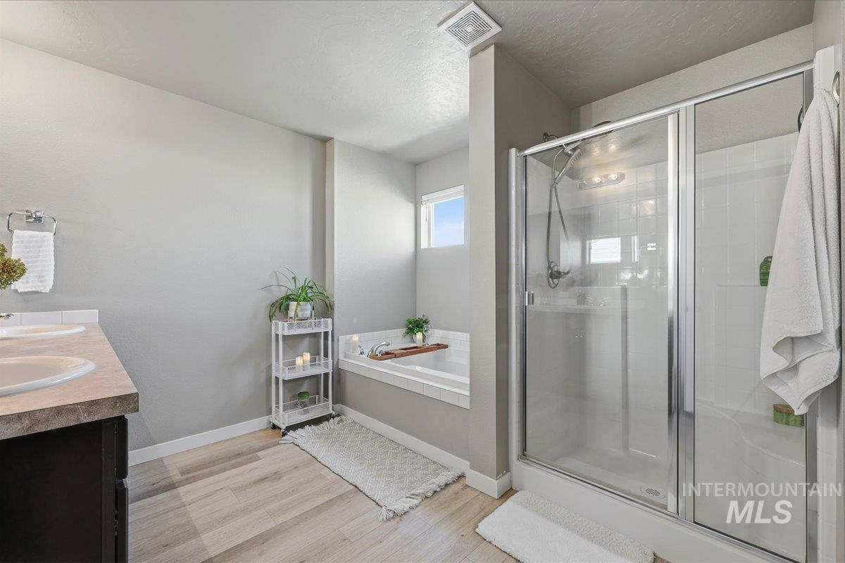 Full bathroom featuring light wood-type flooring, a stall shower, double vanity, a textured ceiling, and a garden tub