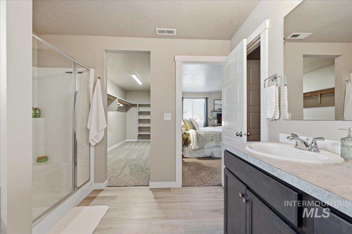Ensuite bathroom with a spacious closet, a stall shower, vanity, light wood-type flooring, and a textured ceiling
