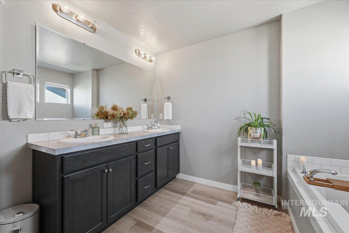 Full bath with double vanity, a garden tub, and light wood-style flooring