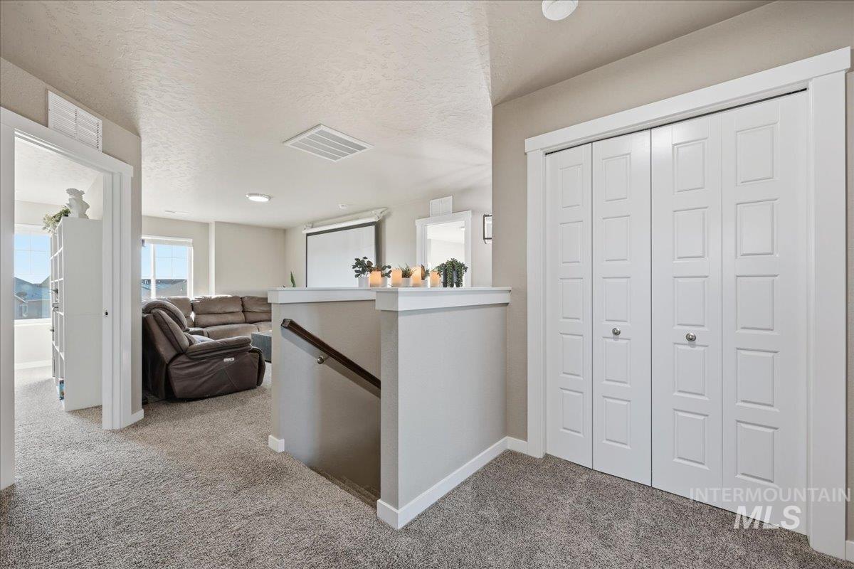 Corridor with an upstairs landing, light carpet, and a textured ceiling