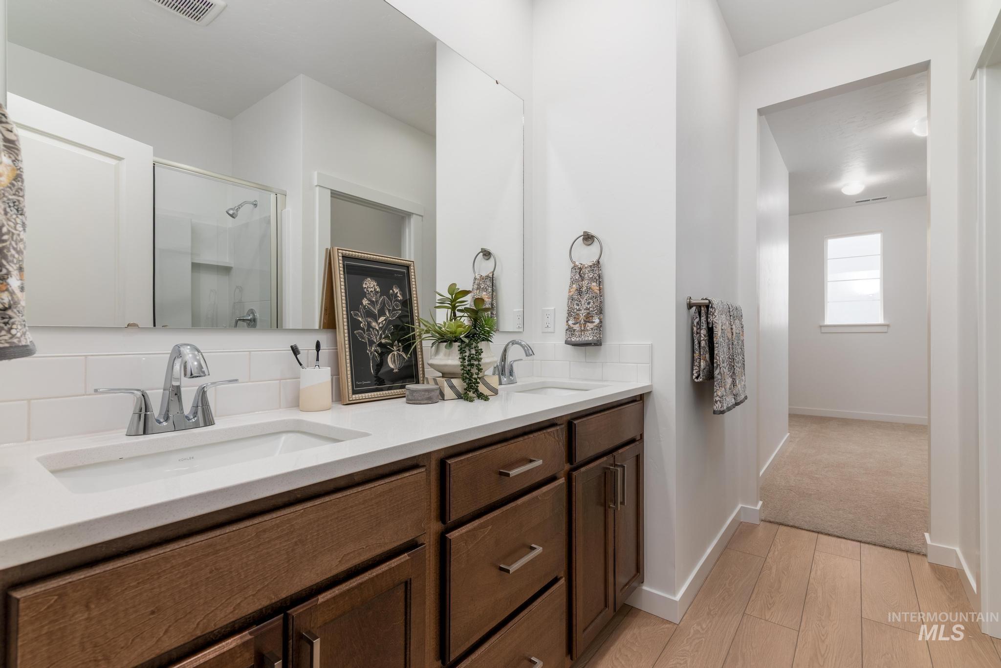 Bathroom featuring a shower stall, tasteful backsplash, double vanity, and light wood-style flooring