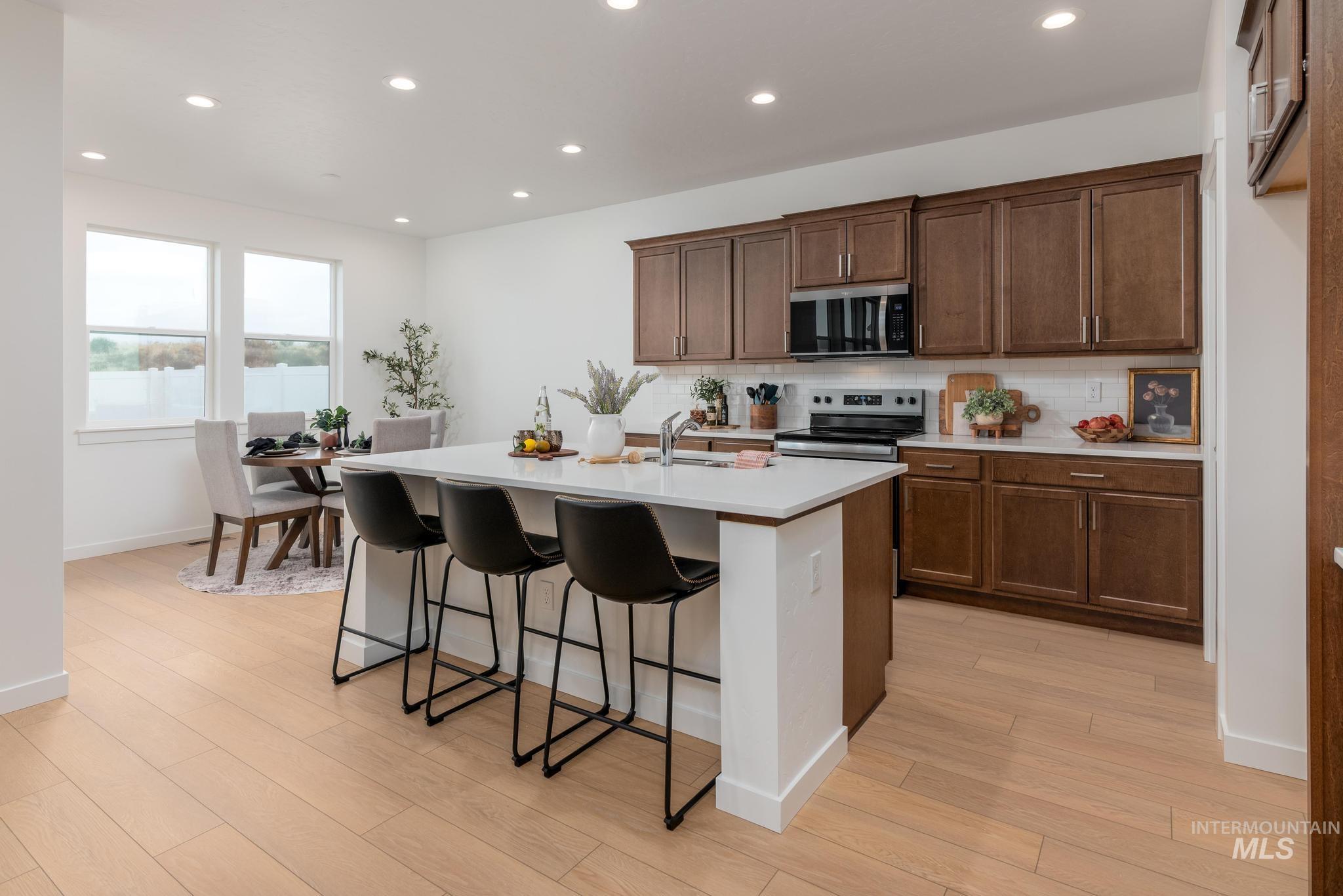 Kitchen featuring a kitchen island with sink, a breakfast bar, stainless steel appliances, recessed lighting, and backsplash