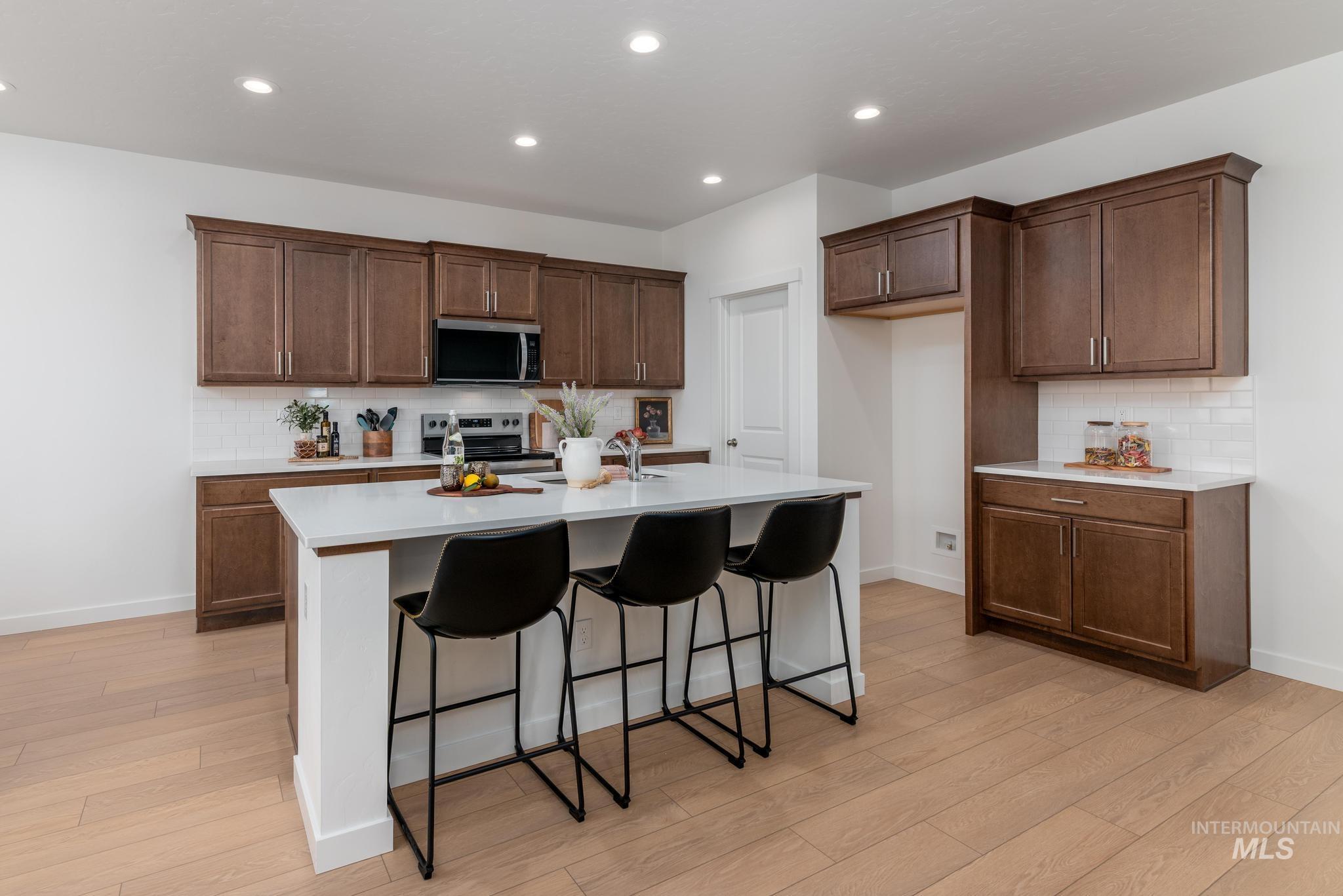 Kitchen with decorative backsplash, a breakfast bar, appliances with stainless steel finishes, a kitchen island with sink, and recessed lighting