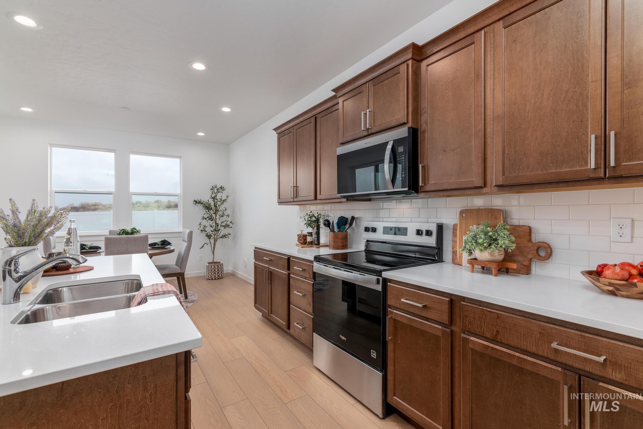 Kitchen featuring stainless steel appliances, recessed lighting, tasteful backsplash, light wood-style floors, and light stone counters