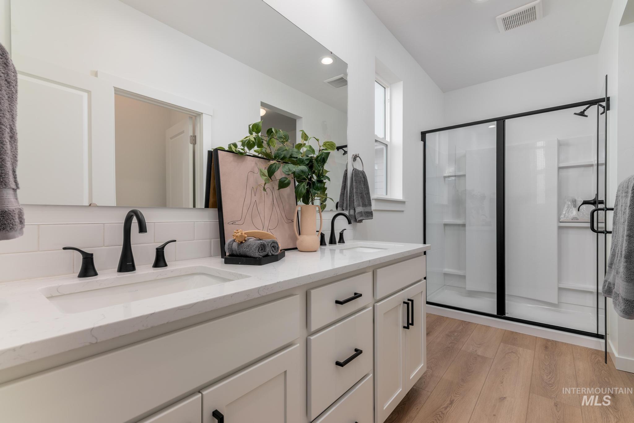 Bathroom with double vanity, light wood-style floors, a stall shower, decorative backsplash, and recessed lighting