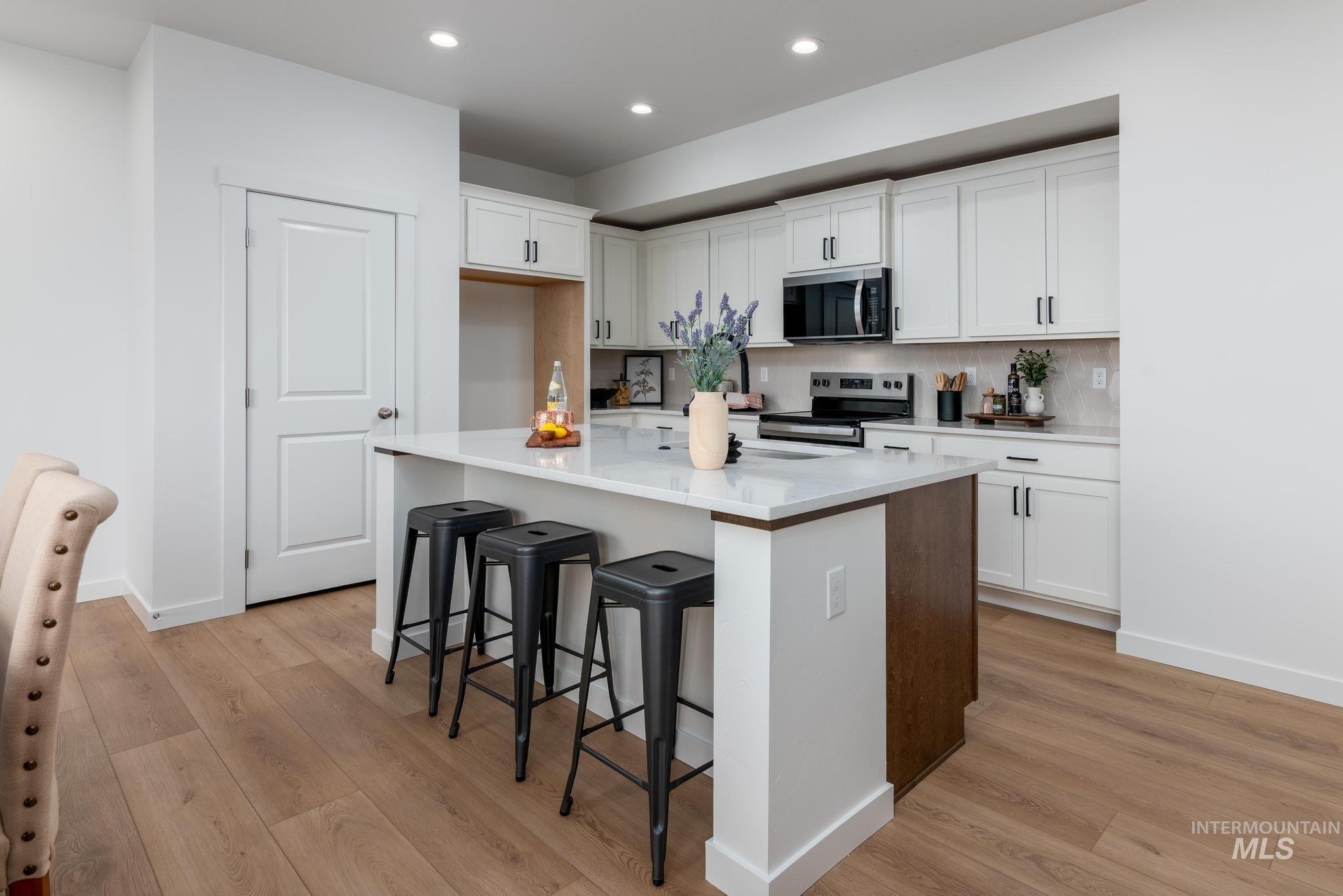 Kitchen with a breakfast bar, white cabinets, a center island with sink, stainless steel appliances, and light wood-style floors