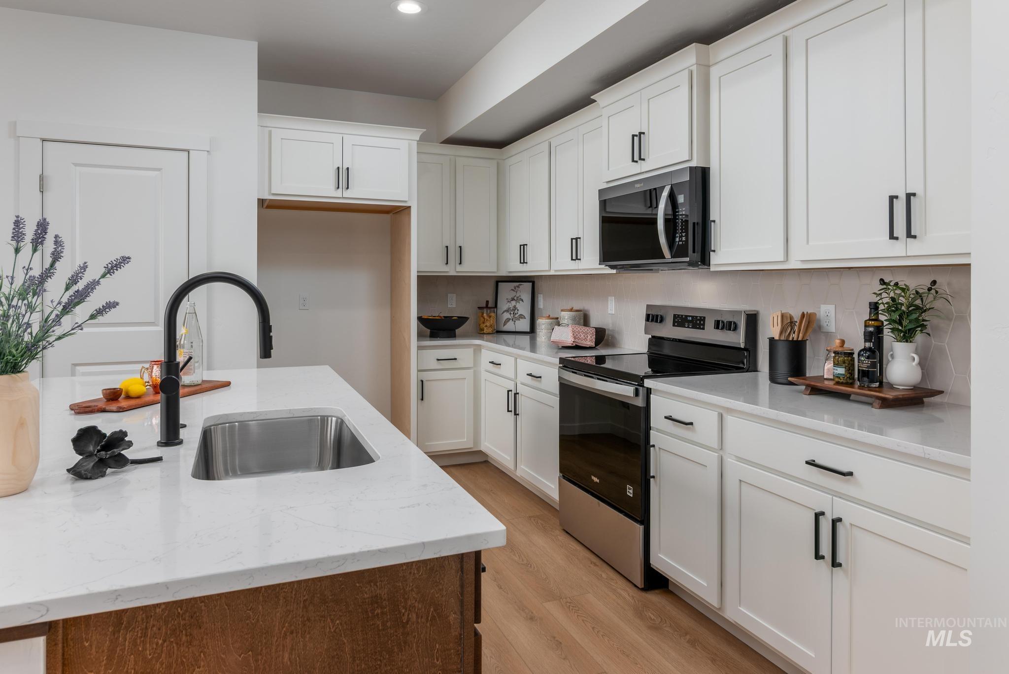 Kitchen with stainless steel electric stove, black microwave, light stone countertops, and white cabinetry