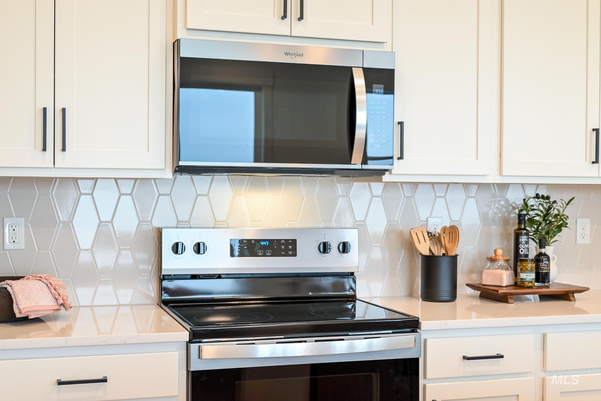 Kitchen featuring appliances with stainless steel finishes, light stone countertops, backsplash, and white cabinets