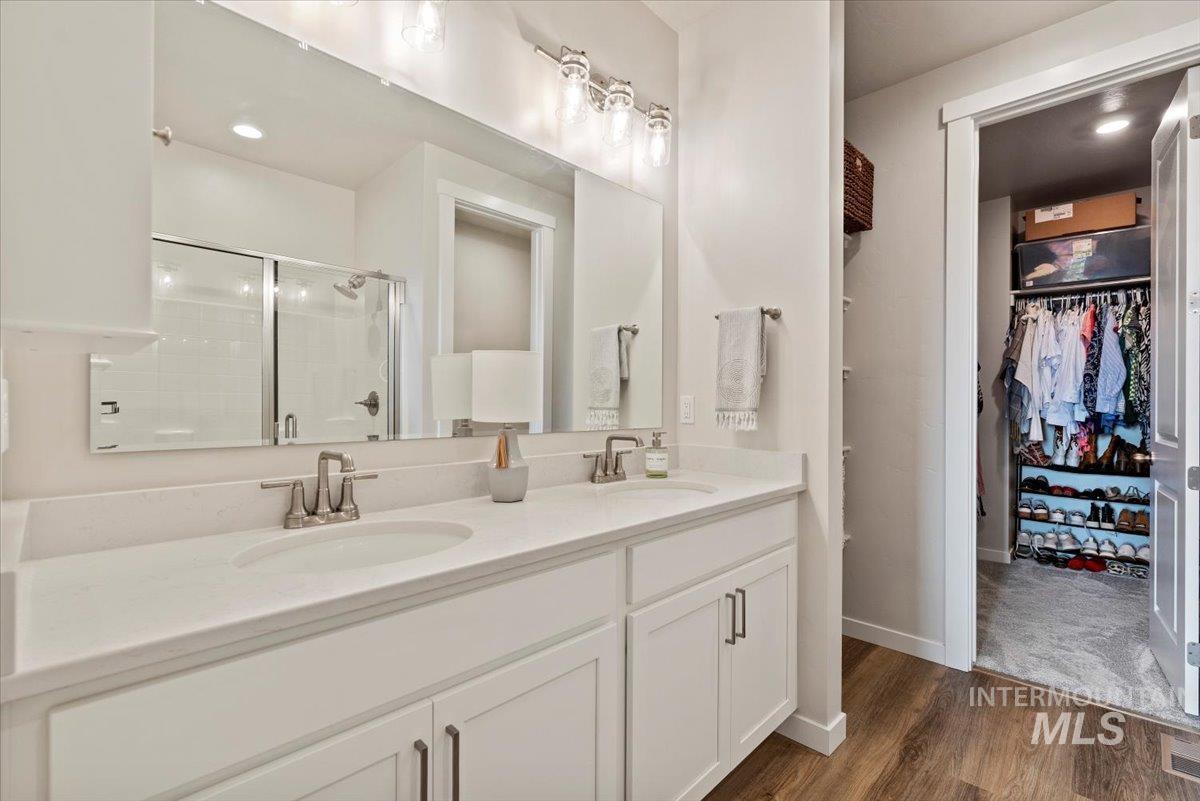 Bathroom with a spacious closet, a stall shower, double vanity, dark wood-style floors, and recessed lighting