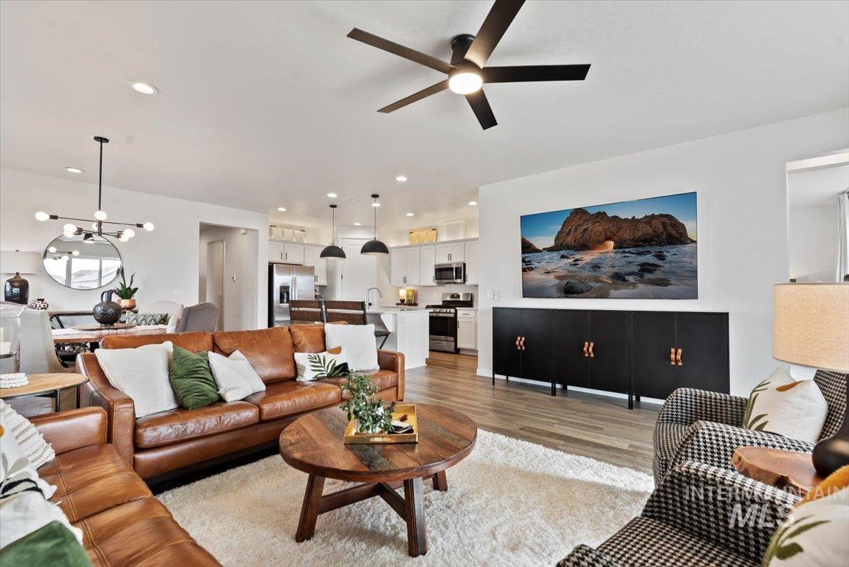 Living area featuring light wood-type flooring, a ceiling fan, a chandelier, and recessed lighting