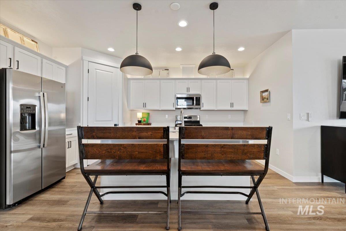 Kitchen with appliances with stainless steel finishes, hanging light fixtures, white cabinetry, a kitchen island with sink, and recessed lighting