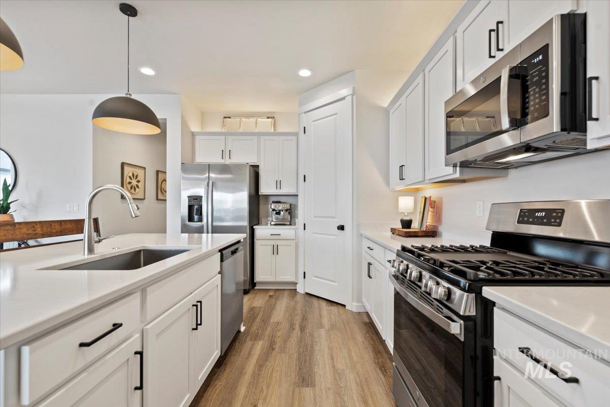 Kitchen featuring appliances with stainless steel finishes, decorative light fixtures, white cabinets, light wood-type flooring, and recessed lighting