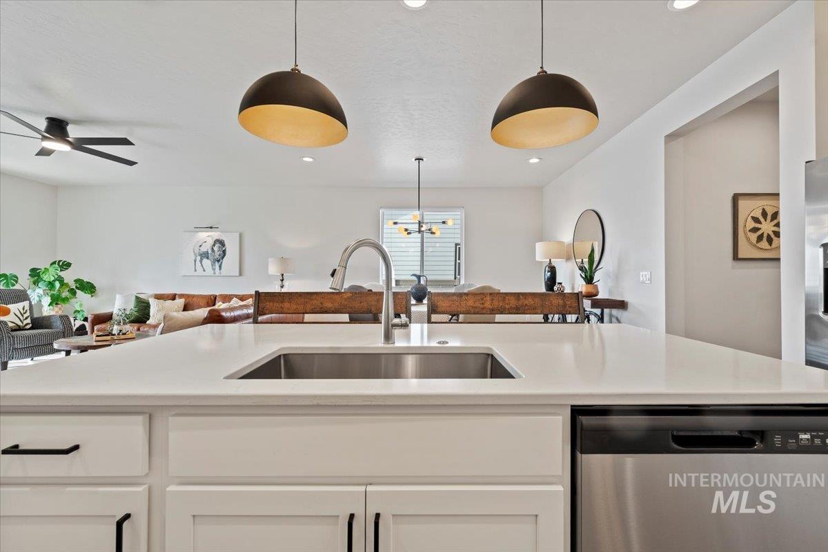 Kitchen featuring dishwasher, open floor plan, white cabinetry, hanging light fixtures, and light stone countertops