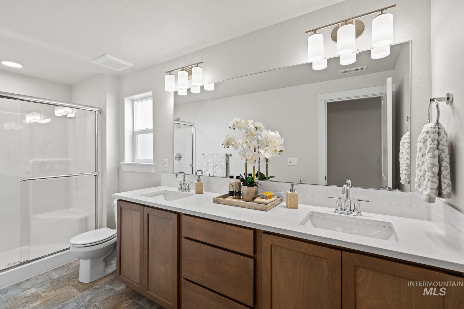 Bathroom with a stall shower, double vanity, and stone finish flooring