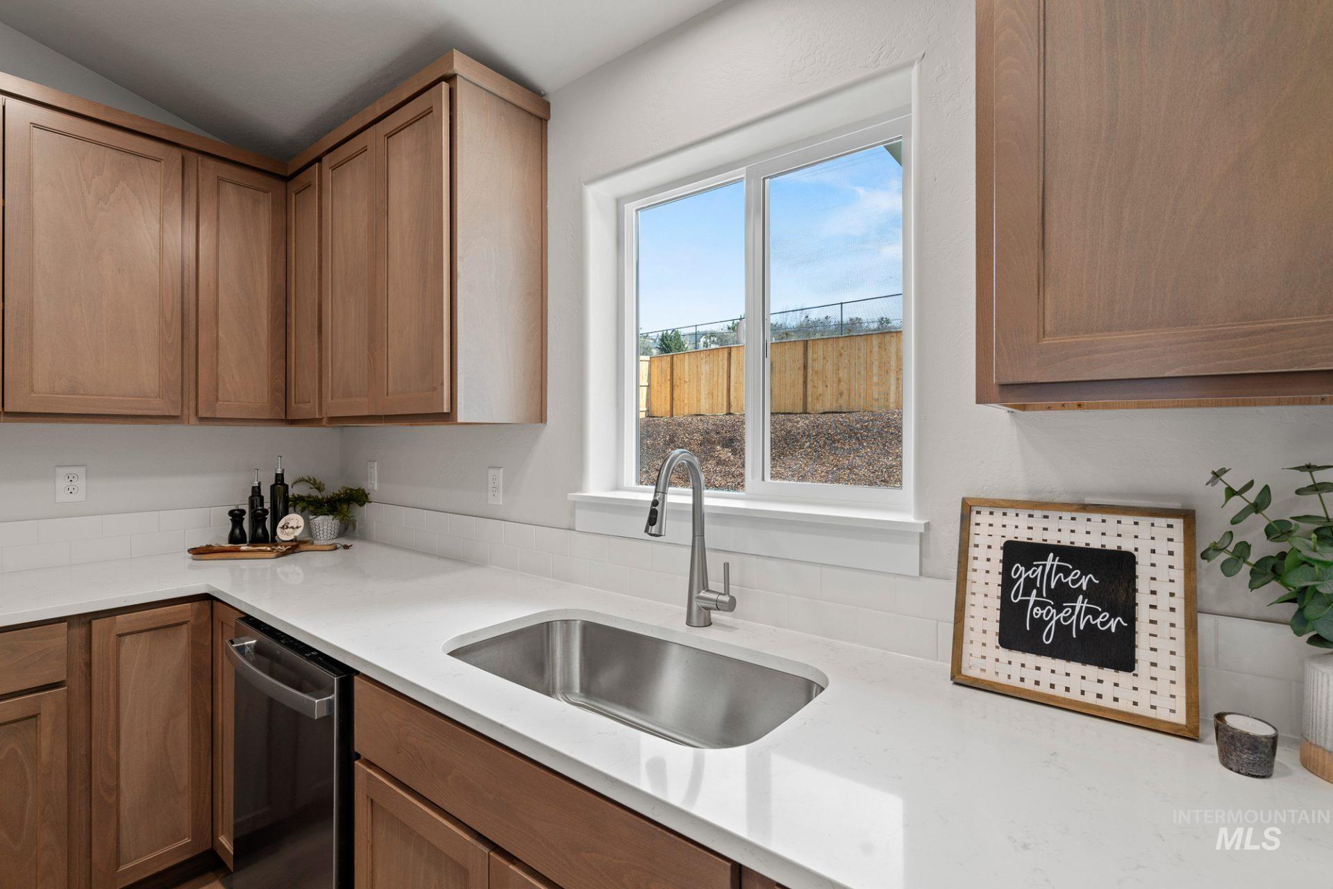 Kitchen with dishwasher, light countertops, brown cabinetry, and vaulted ceiling
