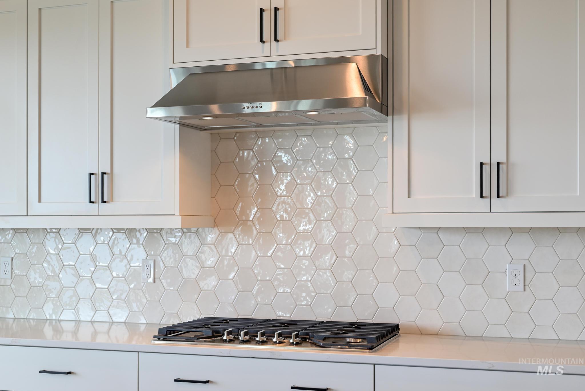 Kitchen featuring white cabinets, under cabinet range hood, backsplash, light stone countertops, and stainless steel gas stovetop