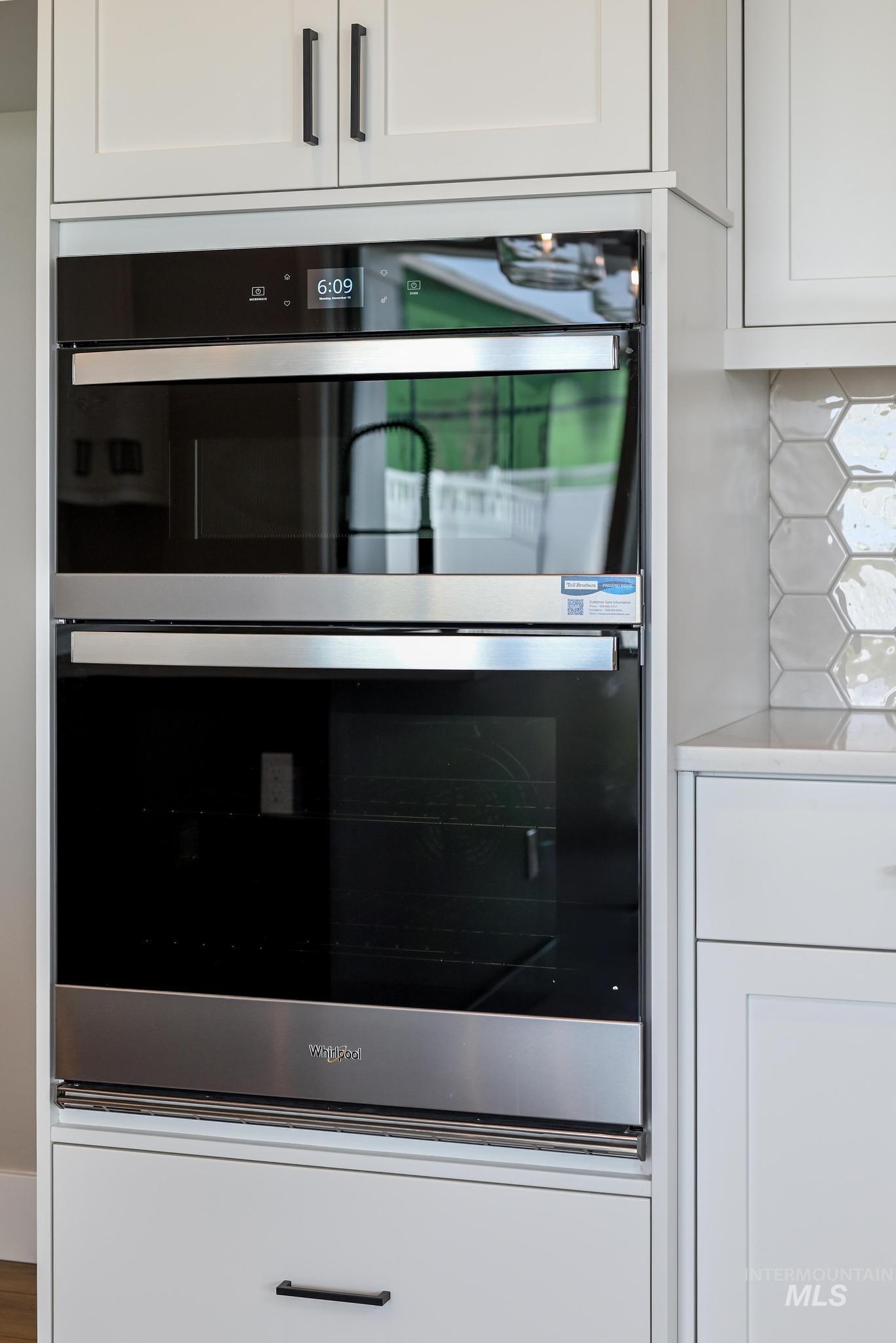 Kitchen view of white cabinetry, stainless steel double oven, and tasteful backsplash