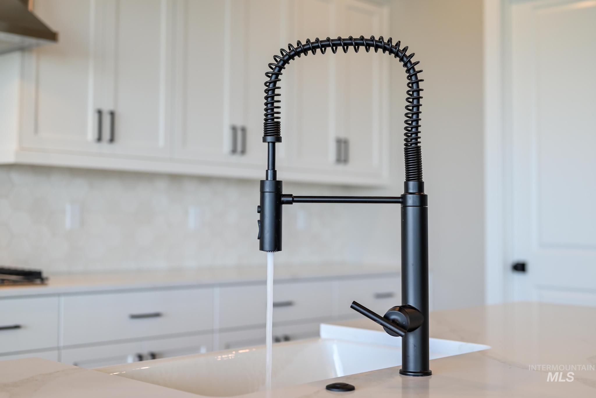 Kitchen view of white cabinetry, light stone countertops, ventilation hood, and backsplash