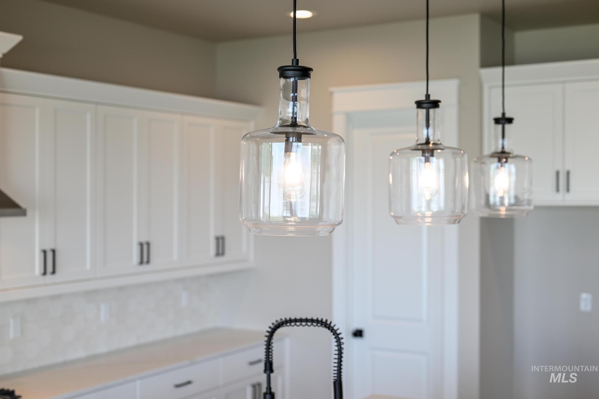 Kitchen view of white cabinets, pendant lighting, and backsplash