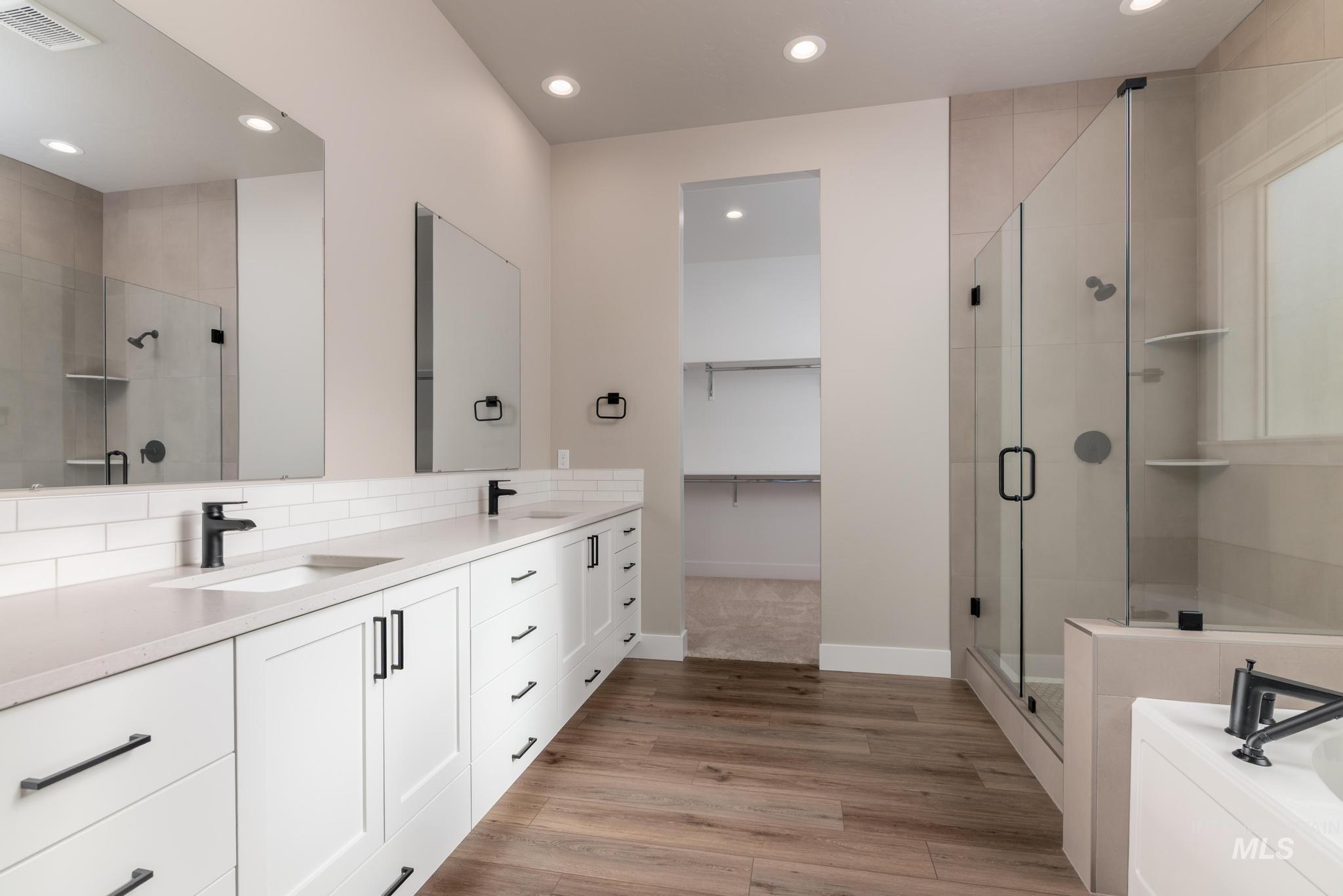 Bathroom with double vanity, a walk in closet, recessed lighting, a shower stall, and light wood-style floors