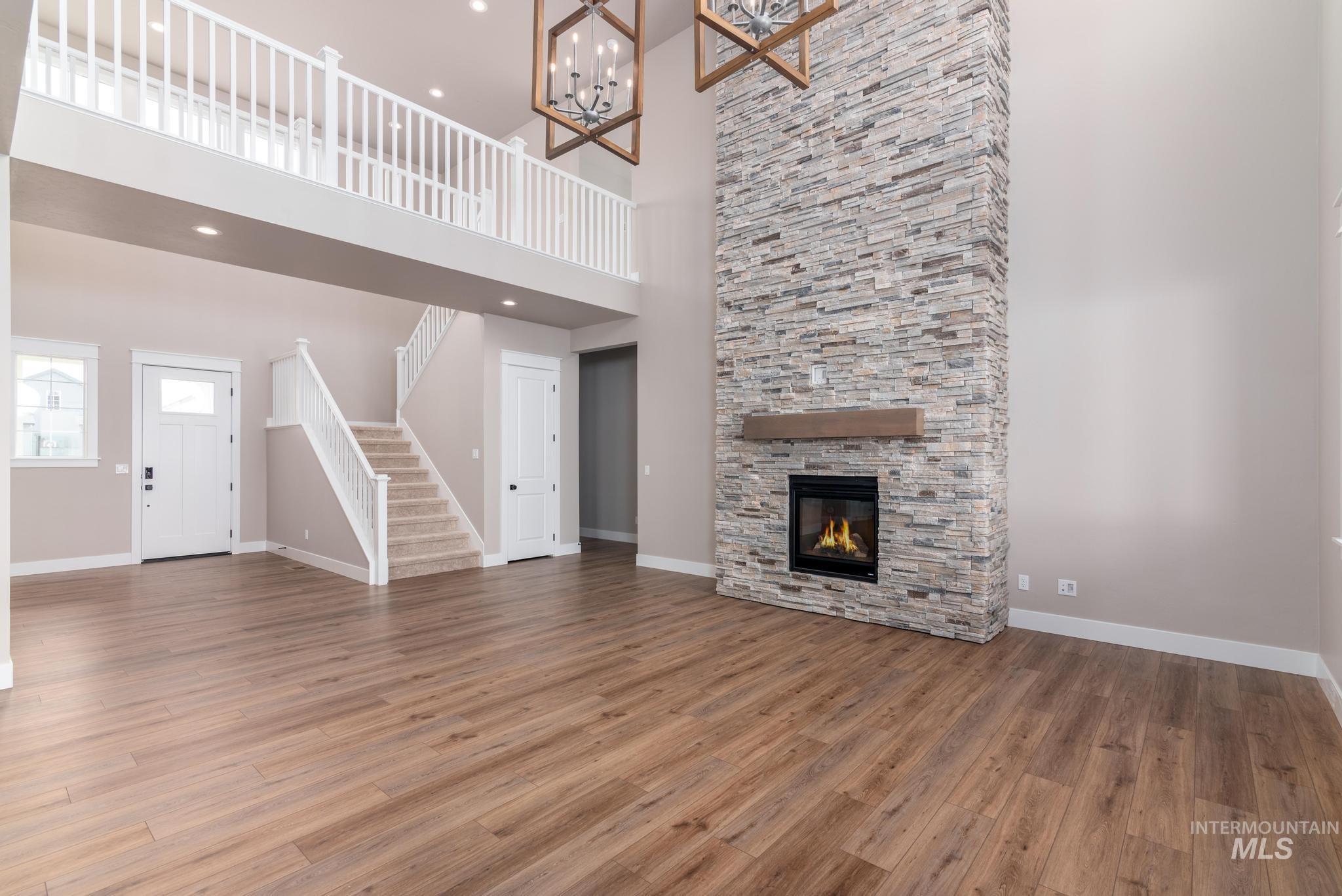 Unfurnished living room with wood finished floors, stairs, a stone fireplace, a chandelier, and a high ceiling