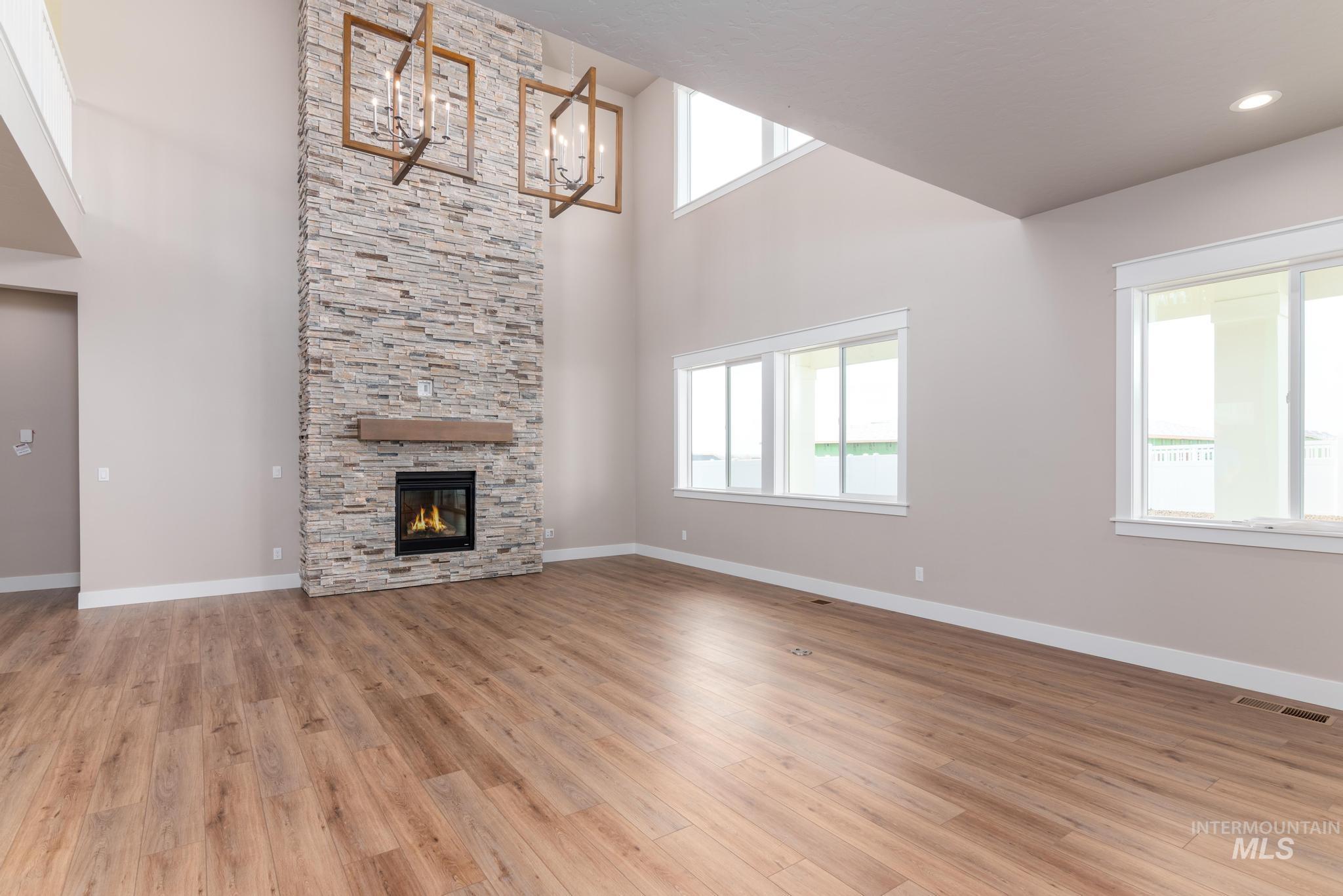 Unfurnished living room with light wood-style flooring, a high ceiling, a chandelier, a fireplace, and plenty of natural light