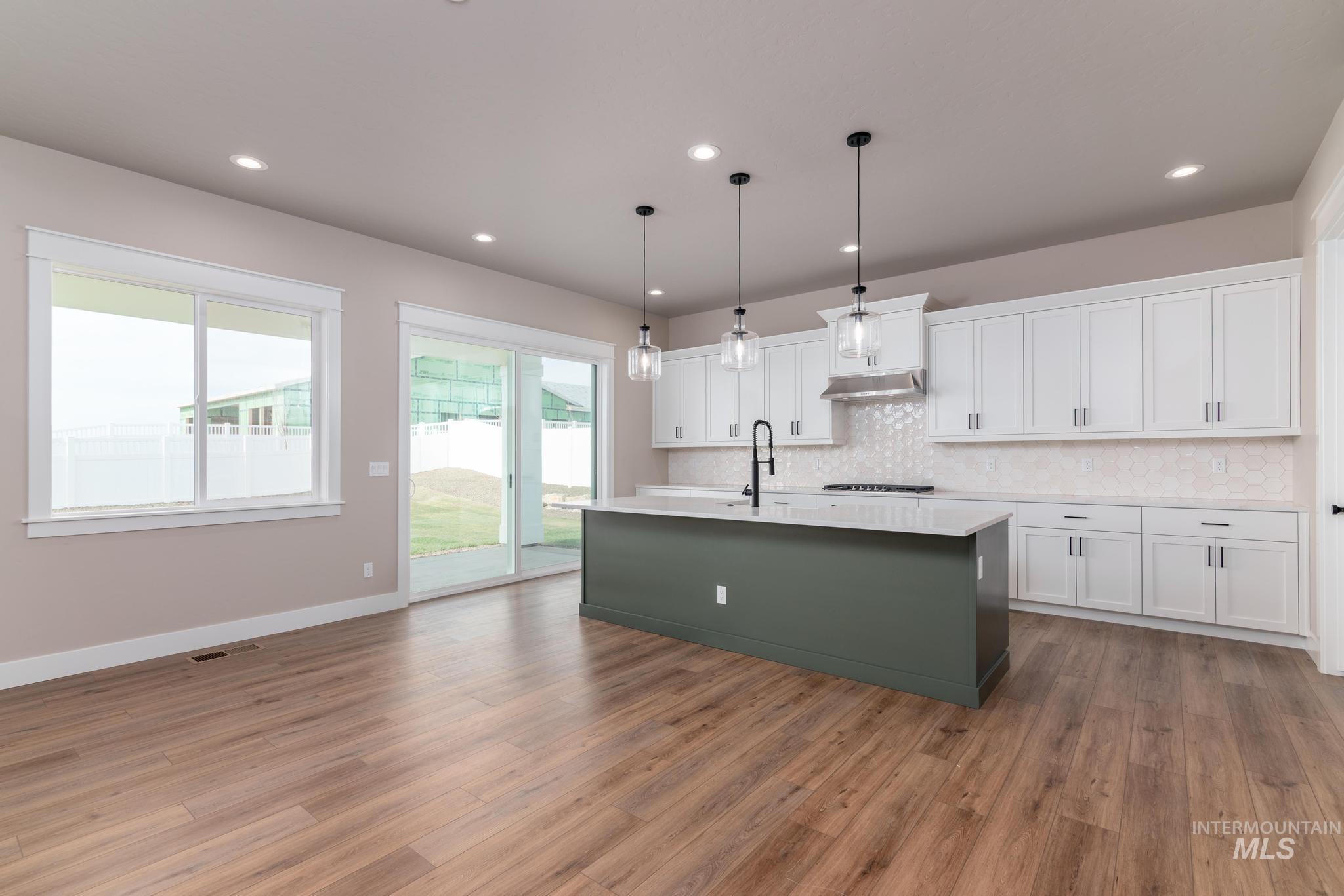 Kitchen with white cabinets, pendant lighting, a kitchen island with sink, light wood-type flooring, and recessed lighting