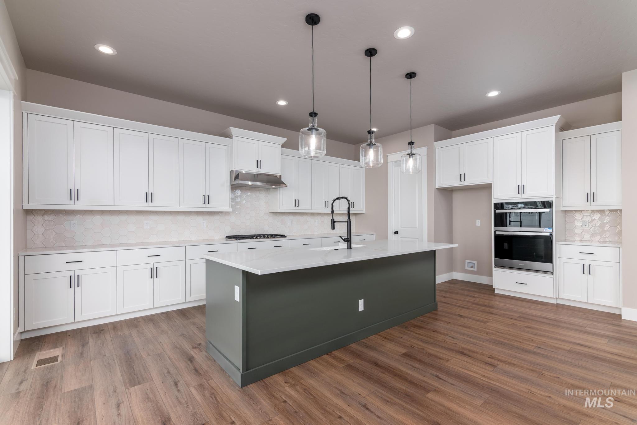 Kitchen featuring tasteful backsplash, white cabinetry, a center island with sink, pendant lighting, and appliances with stainless steel finishes