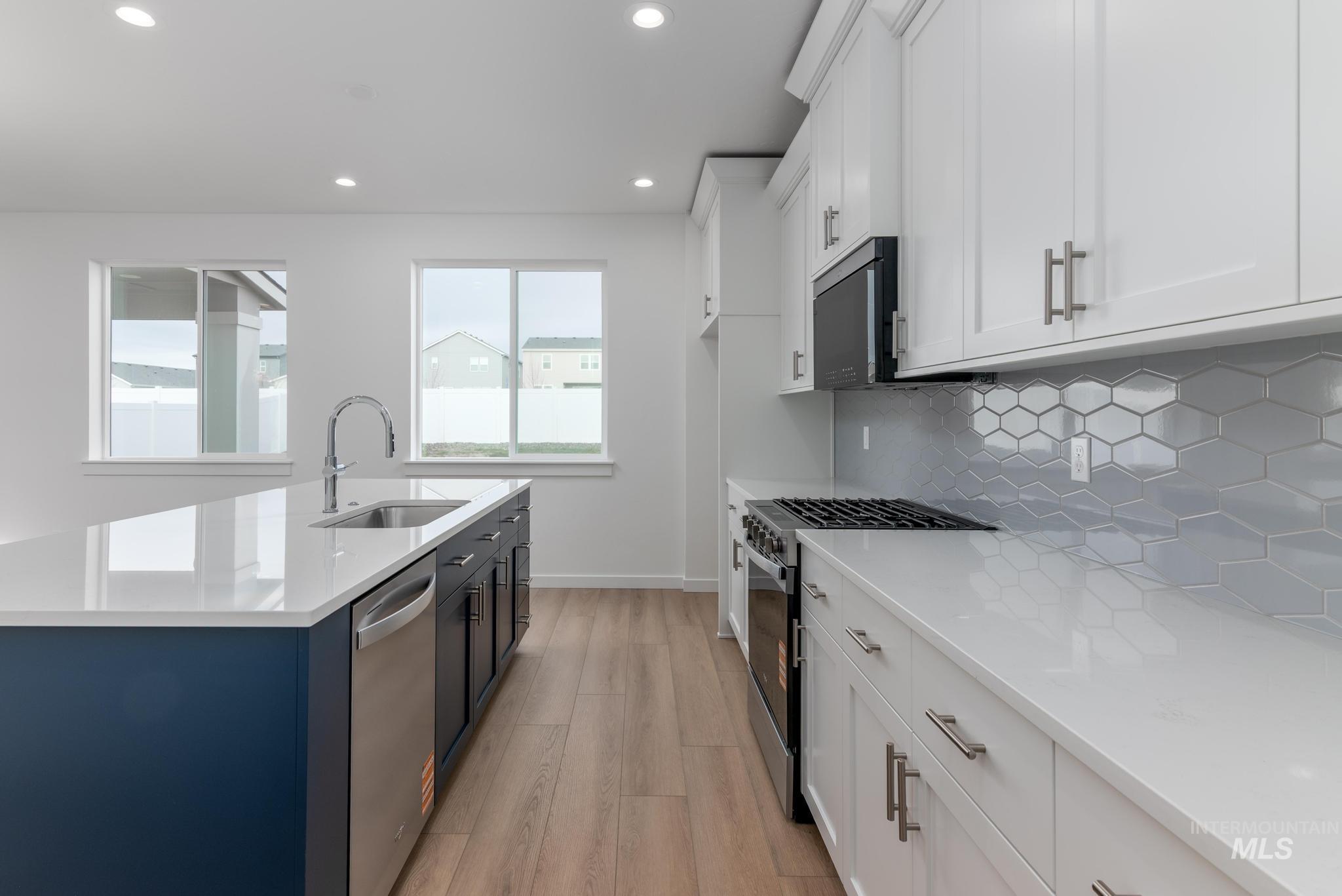 Kitchen featuring white cabinetry, stainless steel appliances, light stone countertops, recessed lighting, and light wood-type flooring