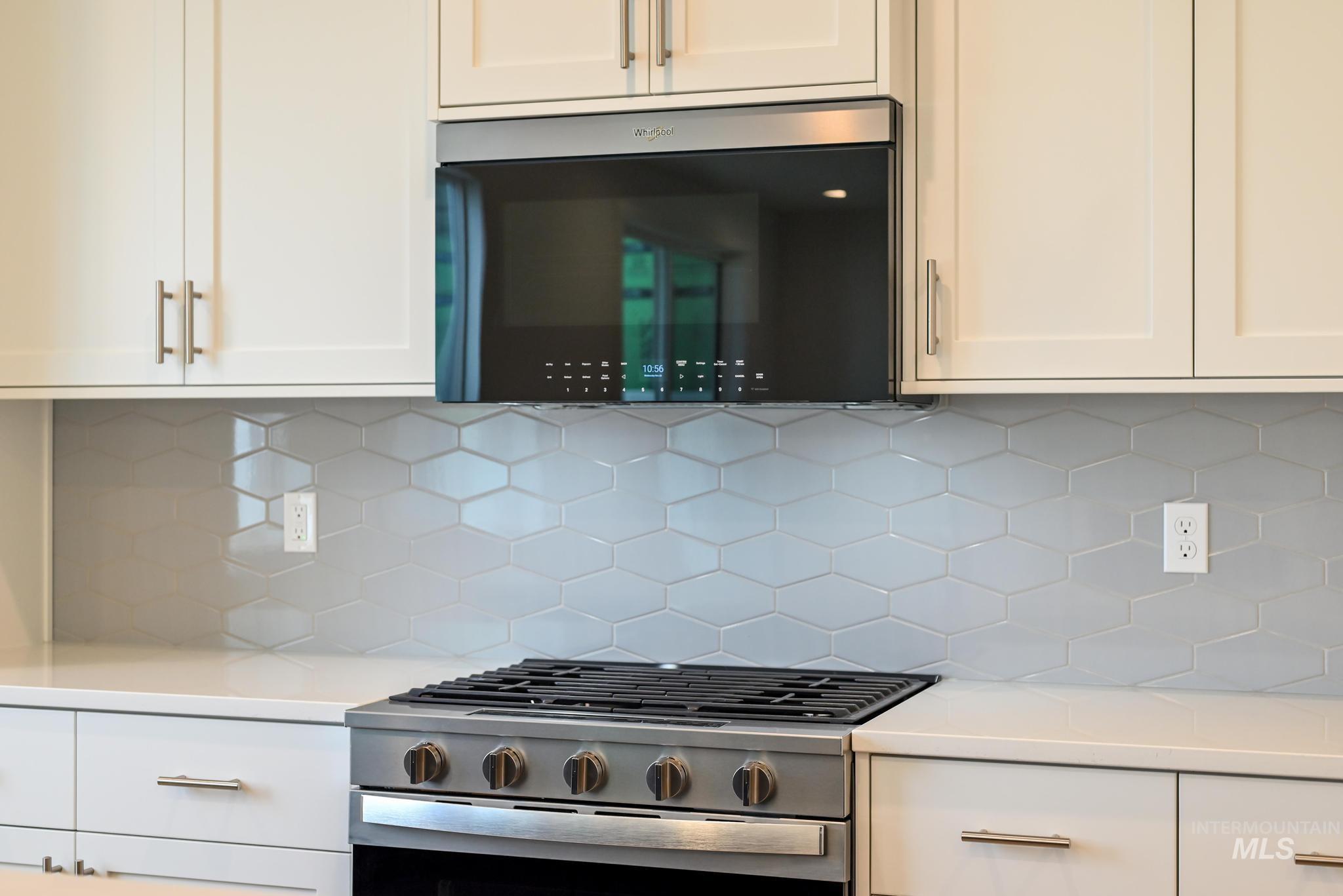 Kitchen featuring white cabinetry, decorative backsplash, stainless steel appliances, and light stone countertops