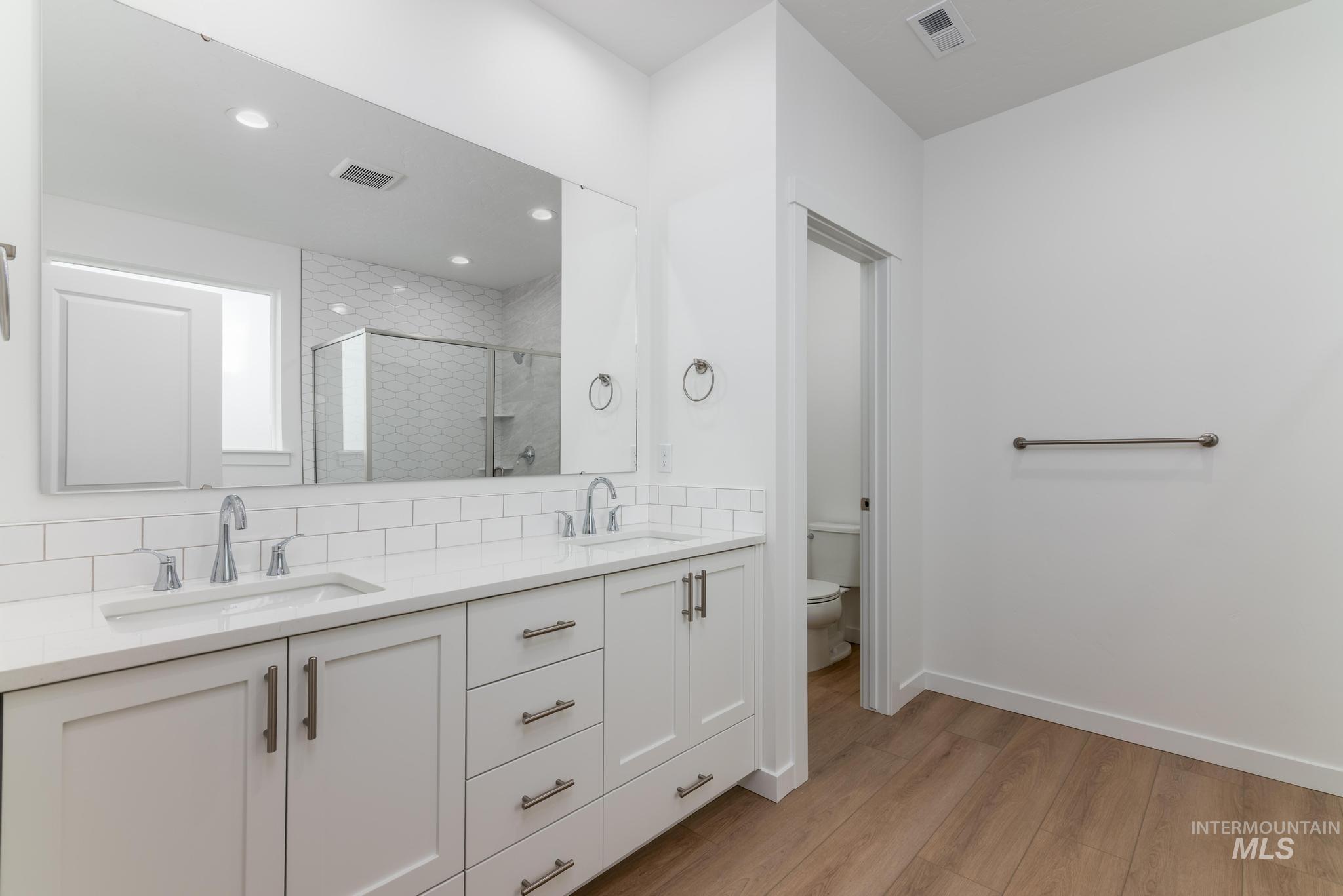 Full bathroom featuring a shower stall, double vanity, light wood-style floors, recessed lighting, and tasteful backsplash