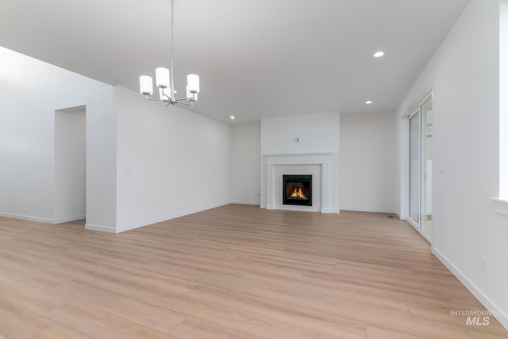 Unfurnished living room with a chandelier, recessed lighting, a lit fireplace, and light wood-style floors