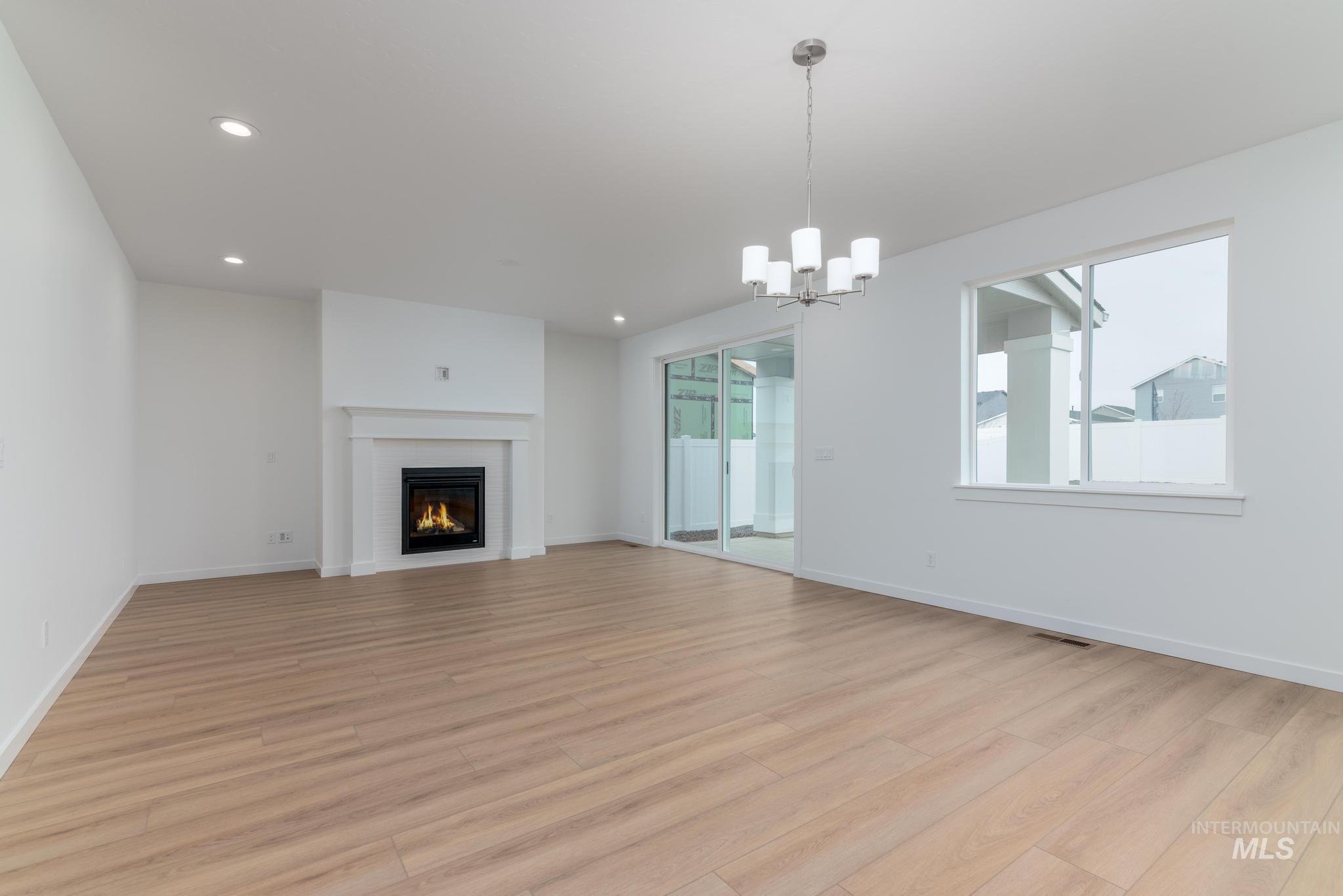 Unfurnished living room featuring light wood-style flooring, a lit fireplace, a chandelier, and recessed lighting