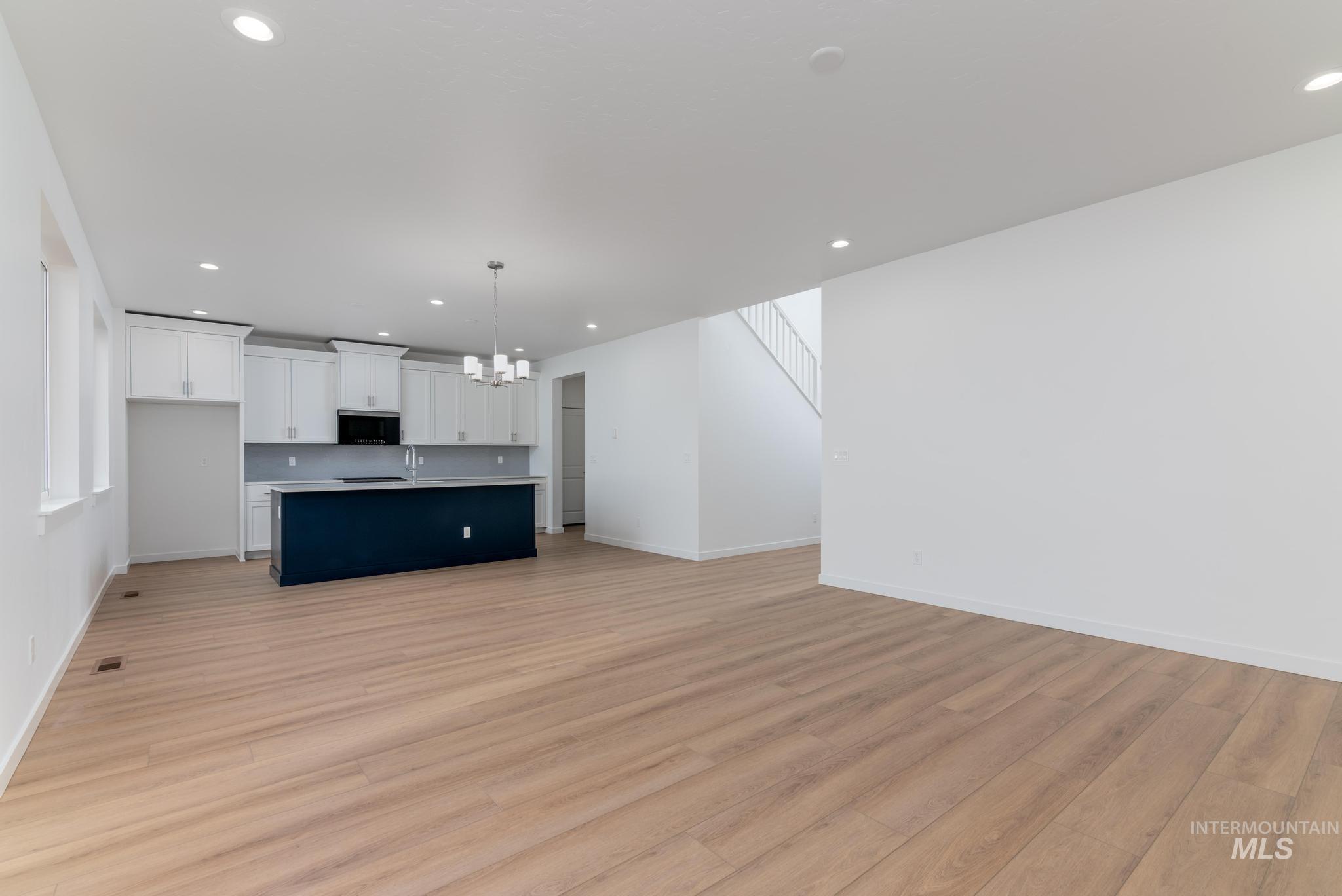 Unfurnished living room featuring recessed lighting, a chandelier, light wood-type flooring, and stairway