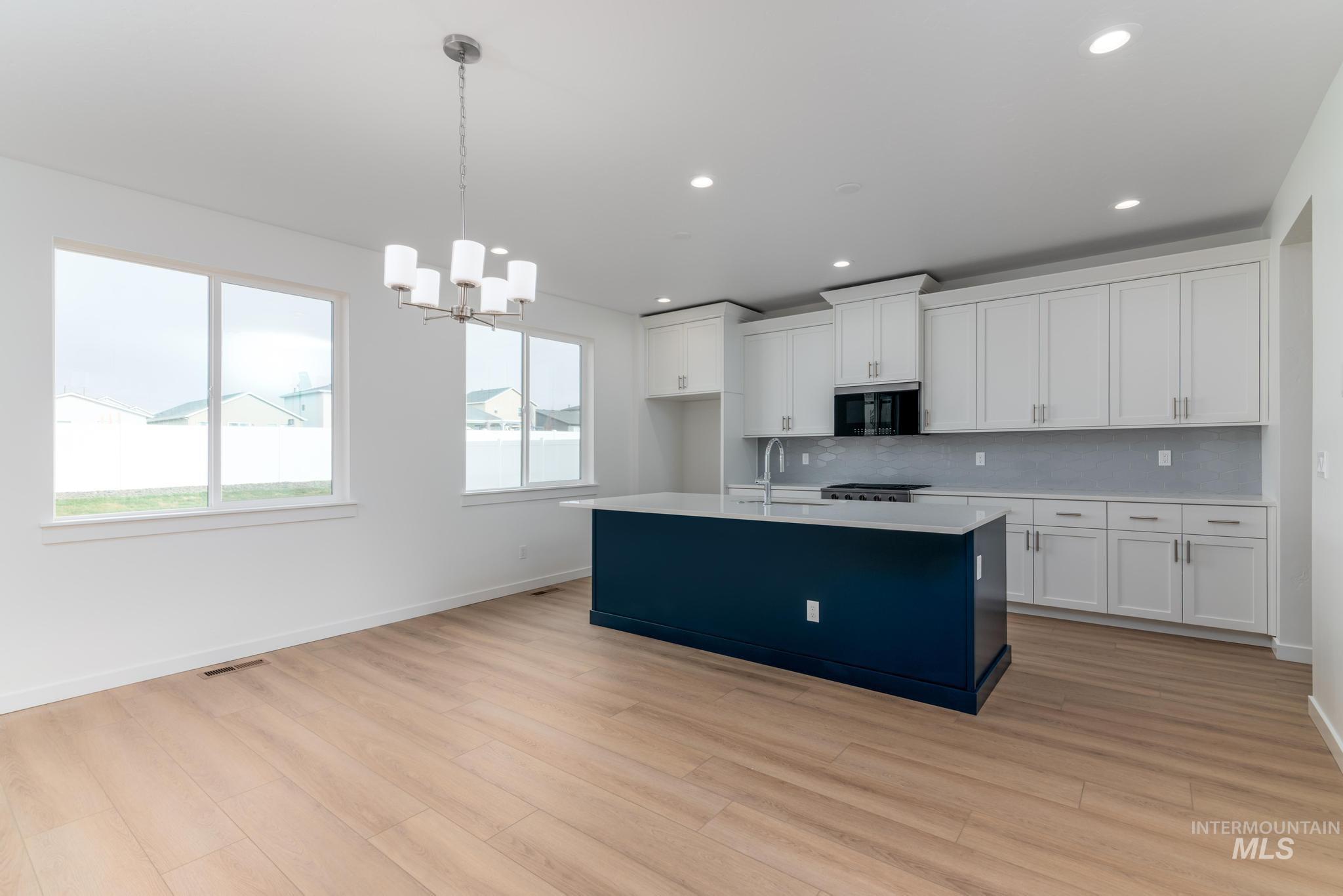 Kitchen featuring white cabinetry, hanging light fixtures, a kitchen island with sink, a chandelier, and decorative backsplash