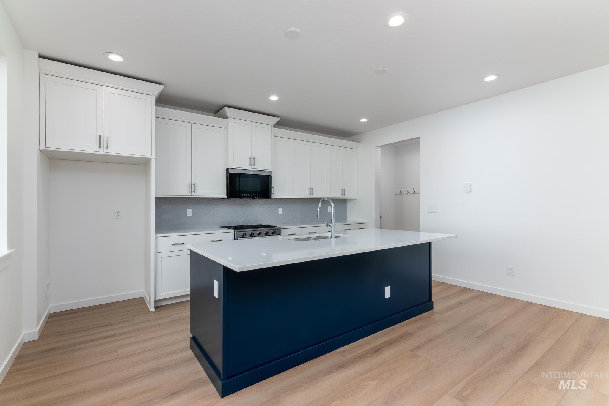 Kitchen featuring white cabinets, an island with sink, light wood-style floors, stainless steel appliances, and recessed lighting