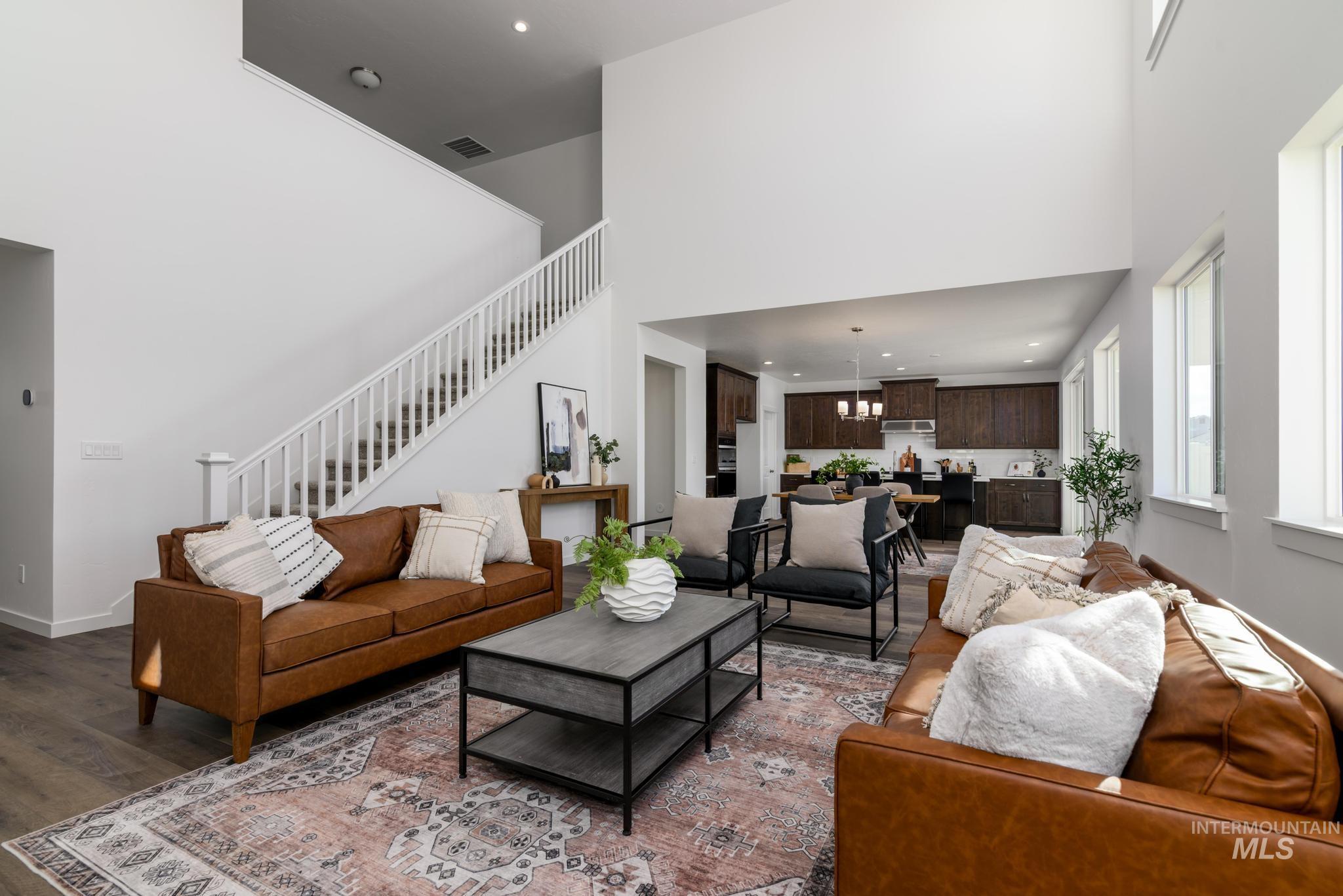 Living area featuring stairway, a chandelier, a towering ceiling, wood finished floors, and recessed lighting