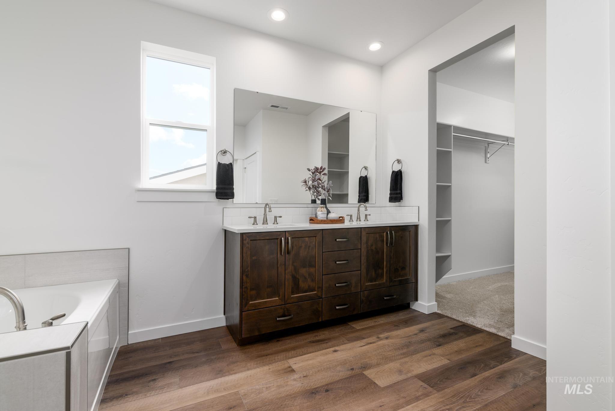 Bathroom with double vanity, a bath, dark wood-style flooring, a walk in closet, and recessed lighting