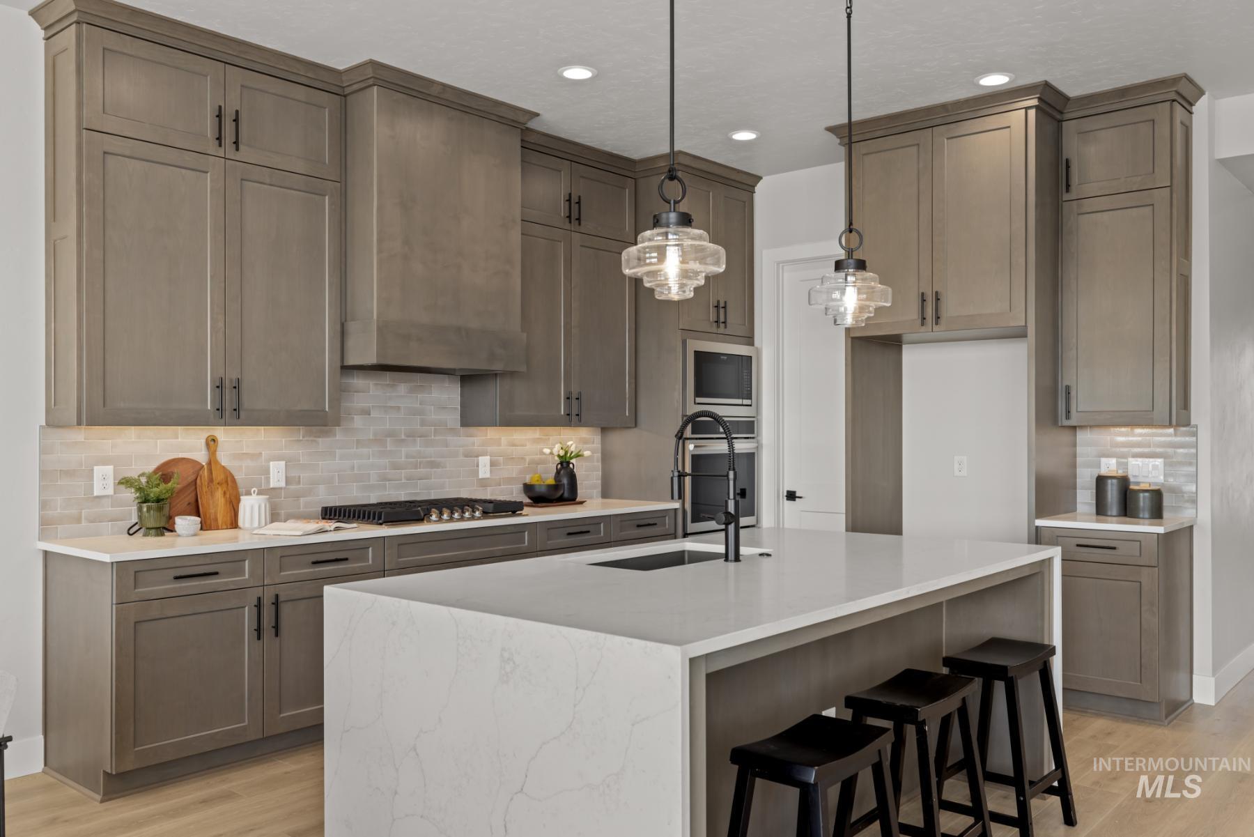 Kitchen with tasteful backsplash, a kitchen breakfast bar, light wood-style flooring, light stone countertops, and a kitchen island with sink