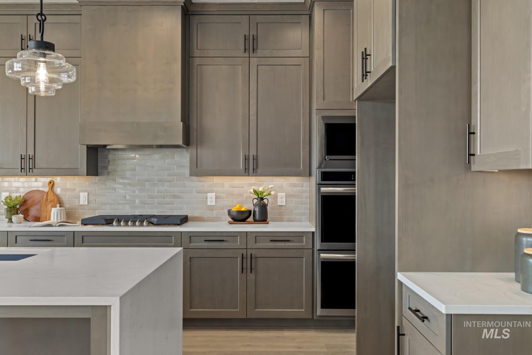 Kitchen featuring decorative backsplash, light stone countertops, appliances with stainless steel finishes, and ventilation hood