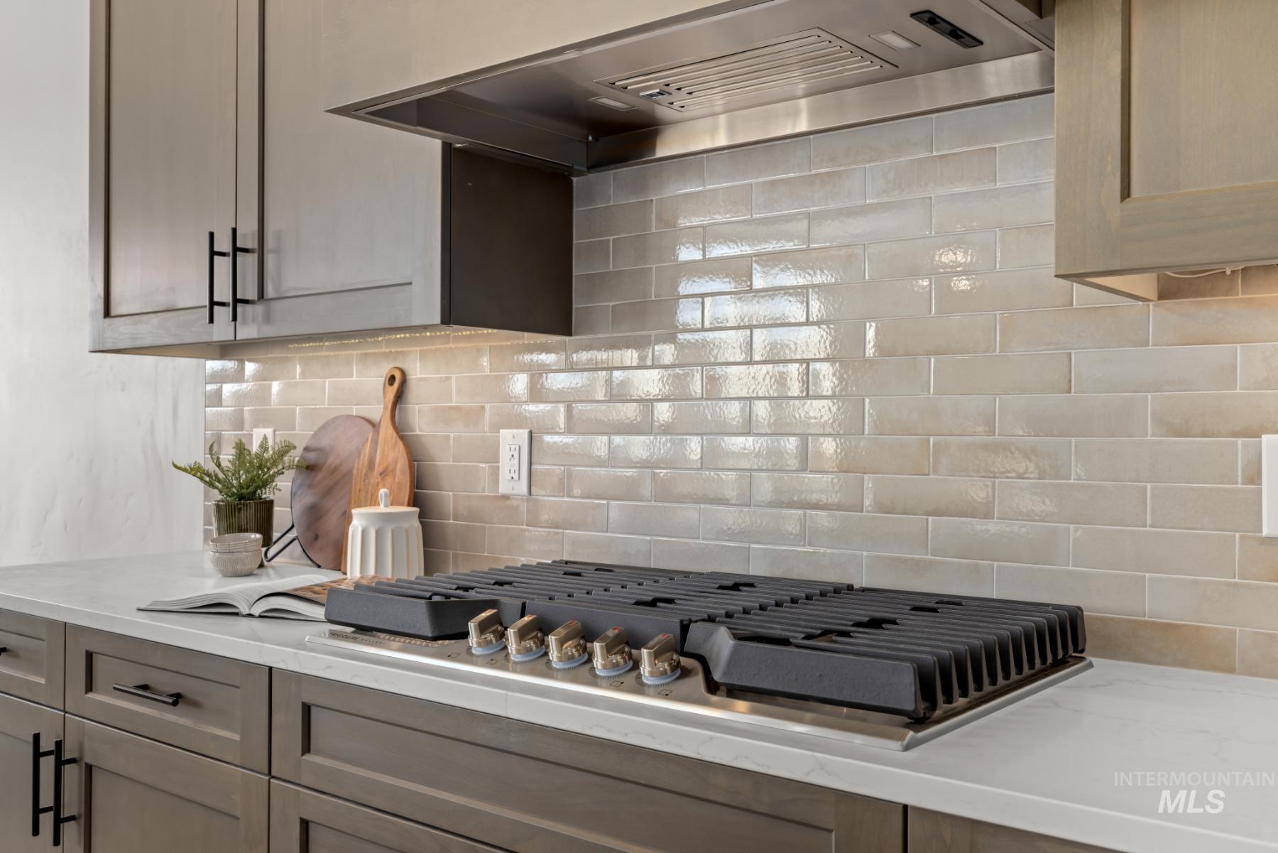 Kitchen with wall chimney range hood, decorative backsplash, stainless steel gas stovetop, and light stone counters