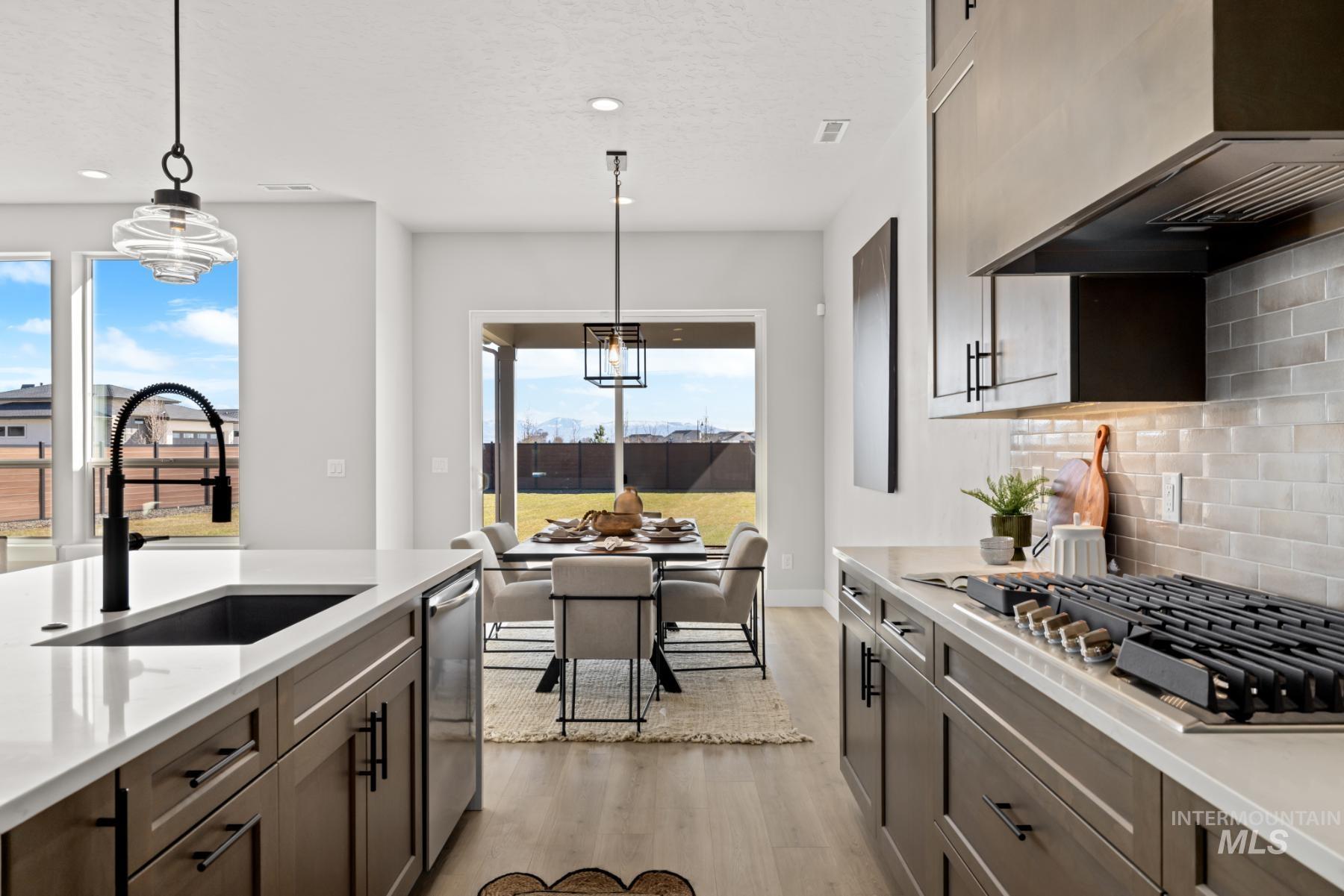 Kitchen with pendant lighting, stainless steel appliances, premium range hood, light wood-style flooring, and light stone counters