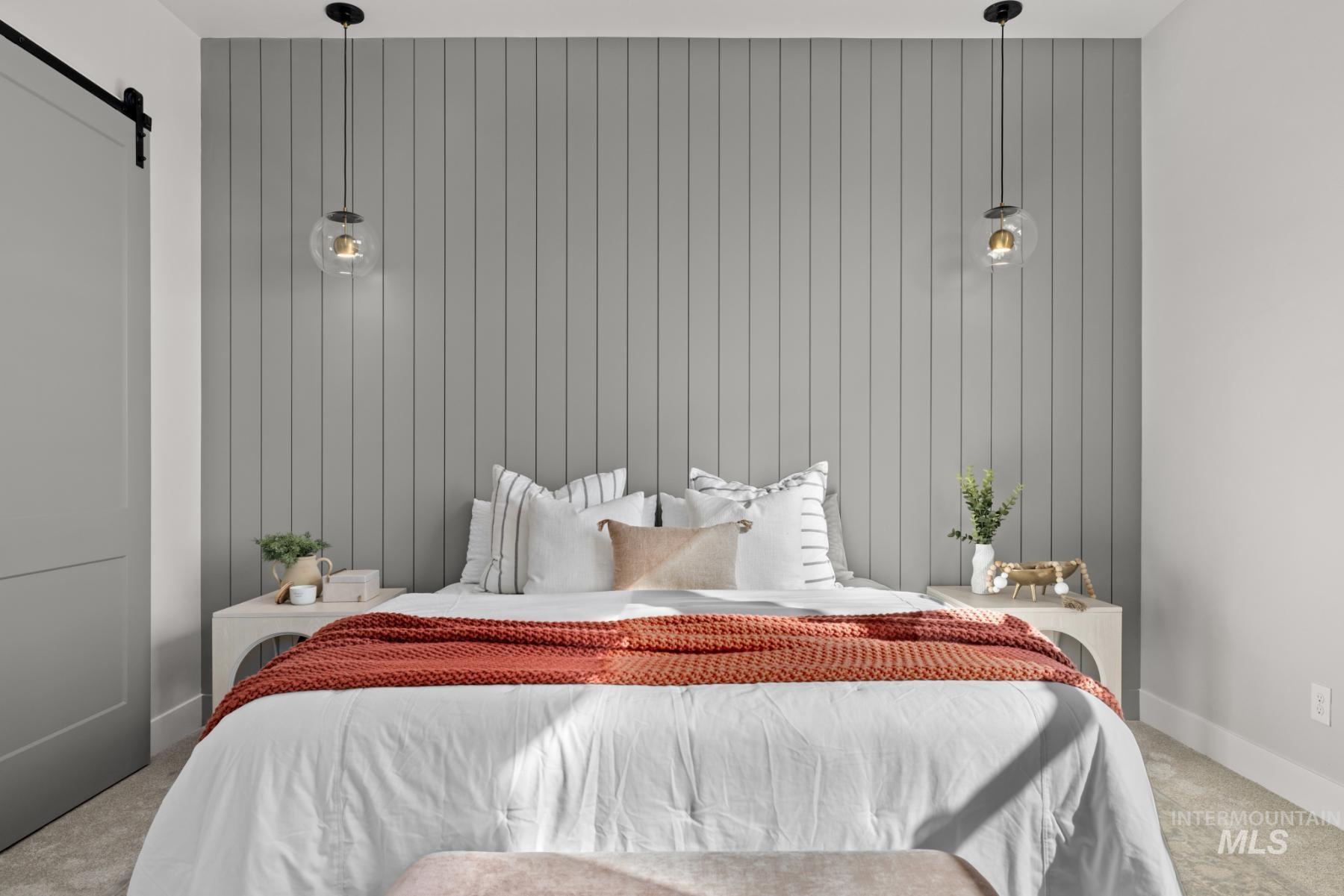 Bedroom with light colored carpet, a barn door, and wood walls