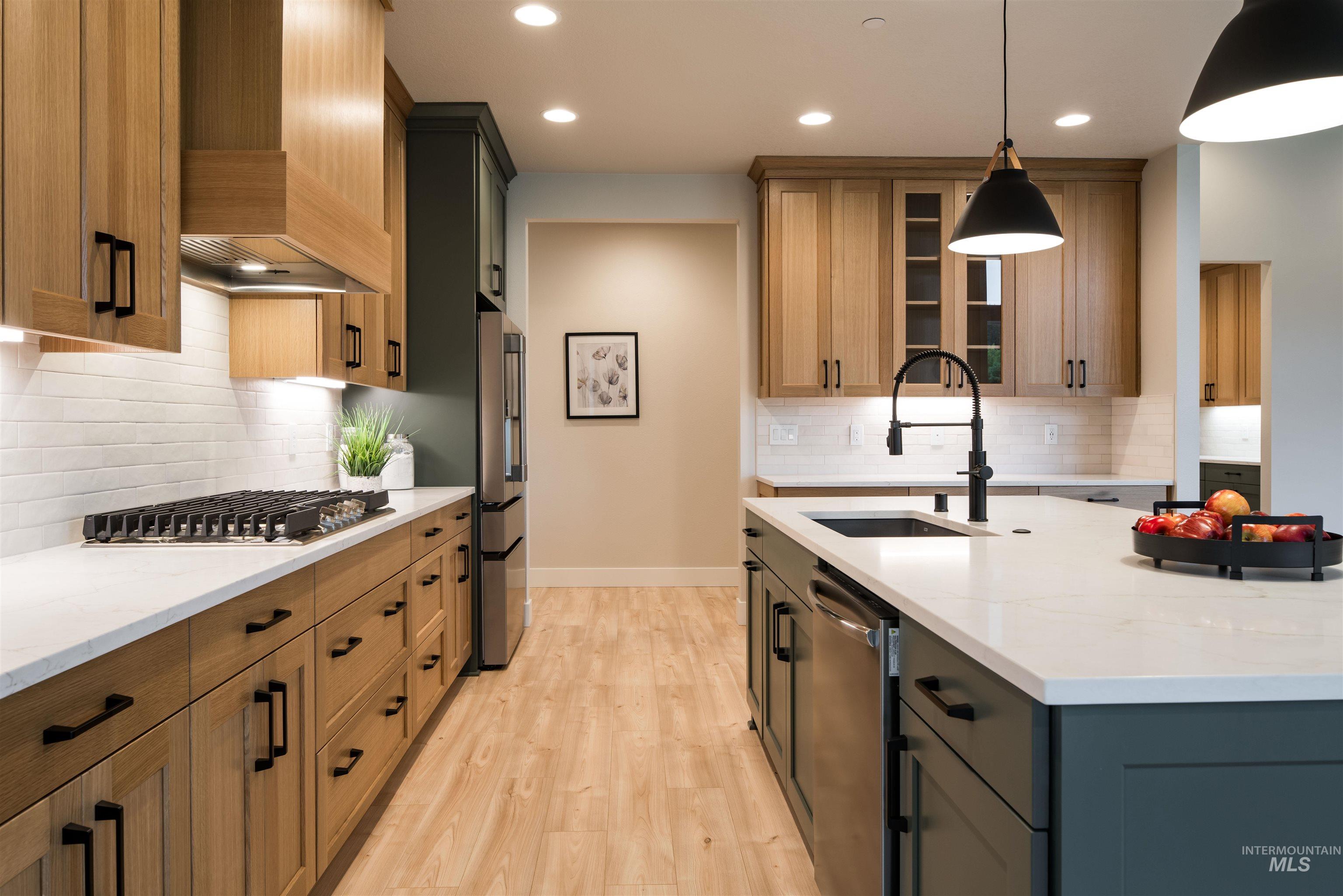Kitchen featuring light stone countertops, decorative backsplash, glass insert cabinets, decorative light fixtures, and light wood-type flooring