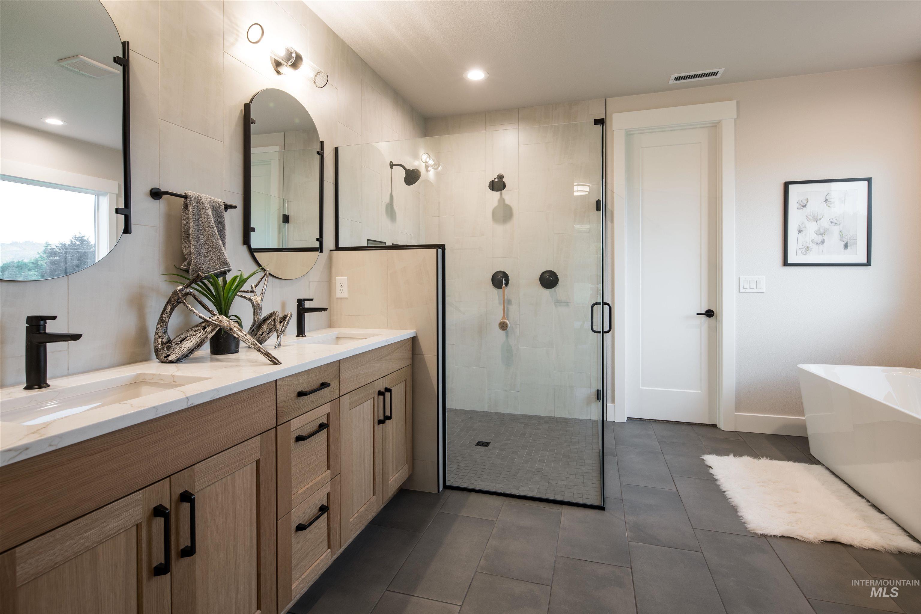 Full bathroom with a stall shower, double vanity, a freestanding bath, dark tile patterned floors, and recessed lighting