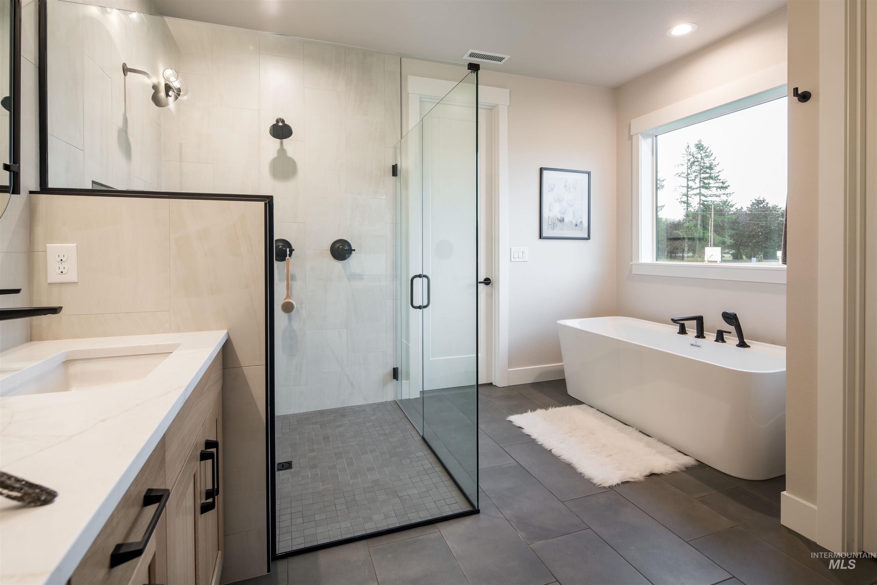 Bathroom featuring a stall shower, a freestanding bath, vanity, dark tile patterned flooring, and recessed lighting