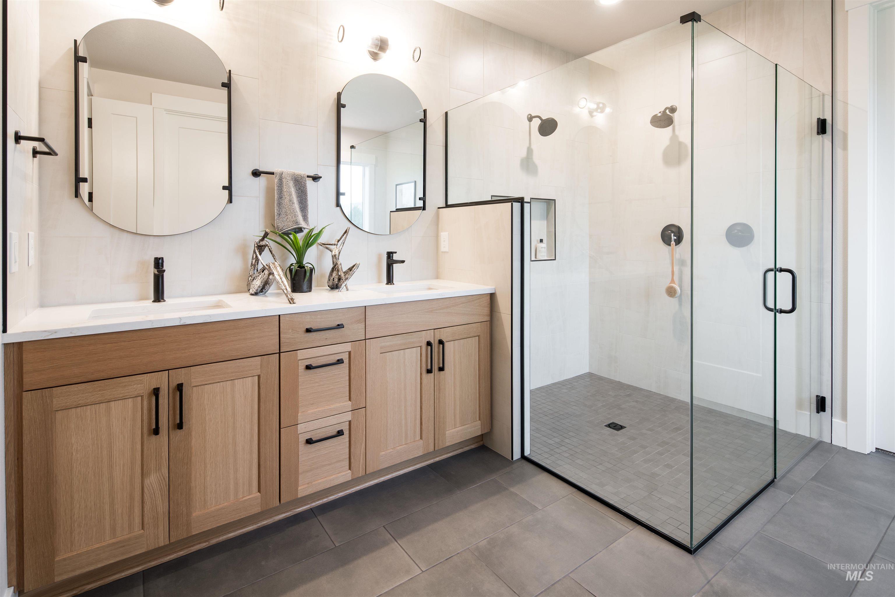Full bathroom with a shower stall, double vanity, and dark tile patterned floors