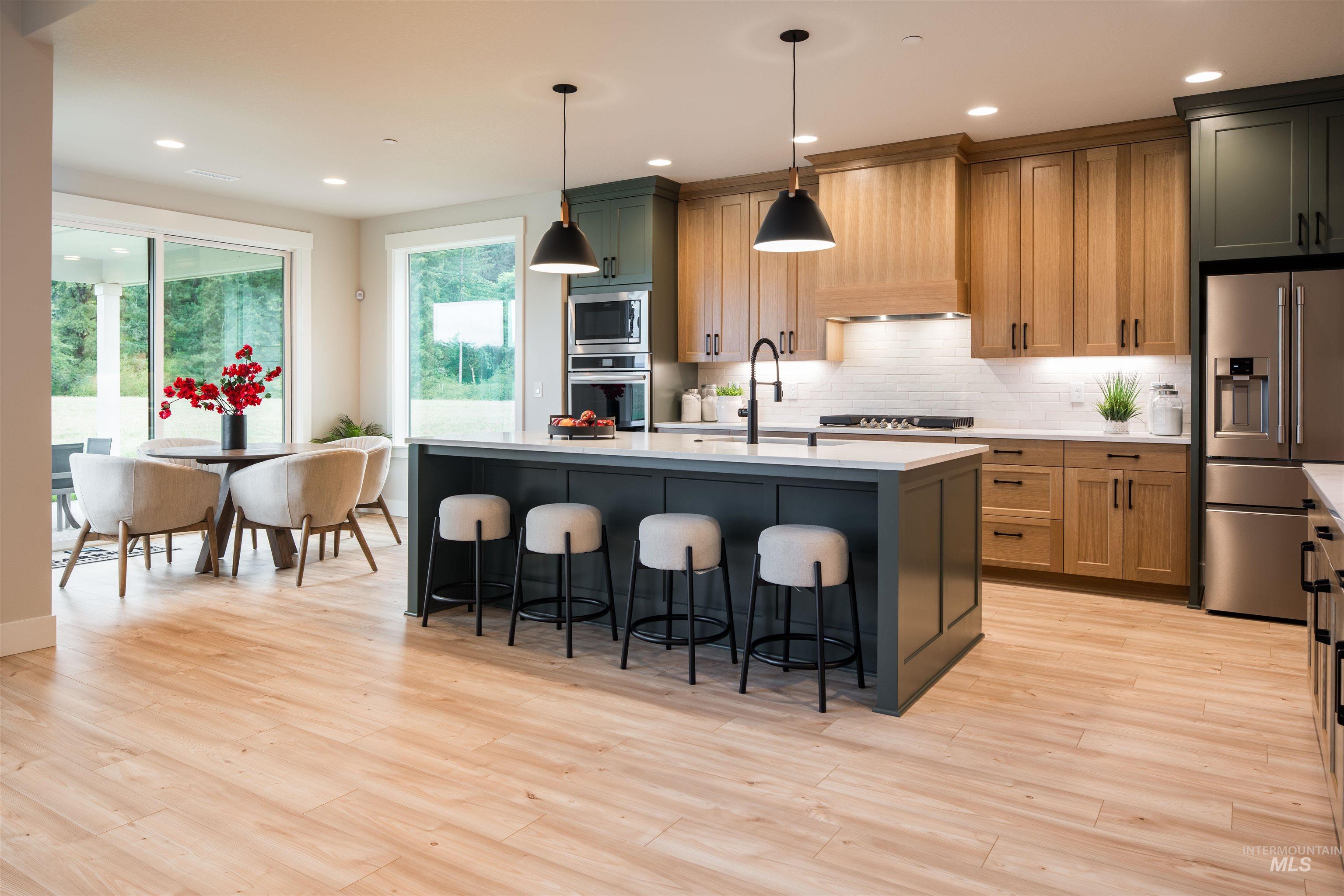 Kitchen featuring appliances with stainless steel finishes, tasteful backsplash, a breakfast bar, decorative light fixtures, and an island with sink